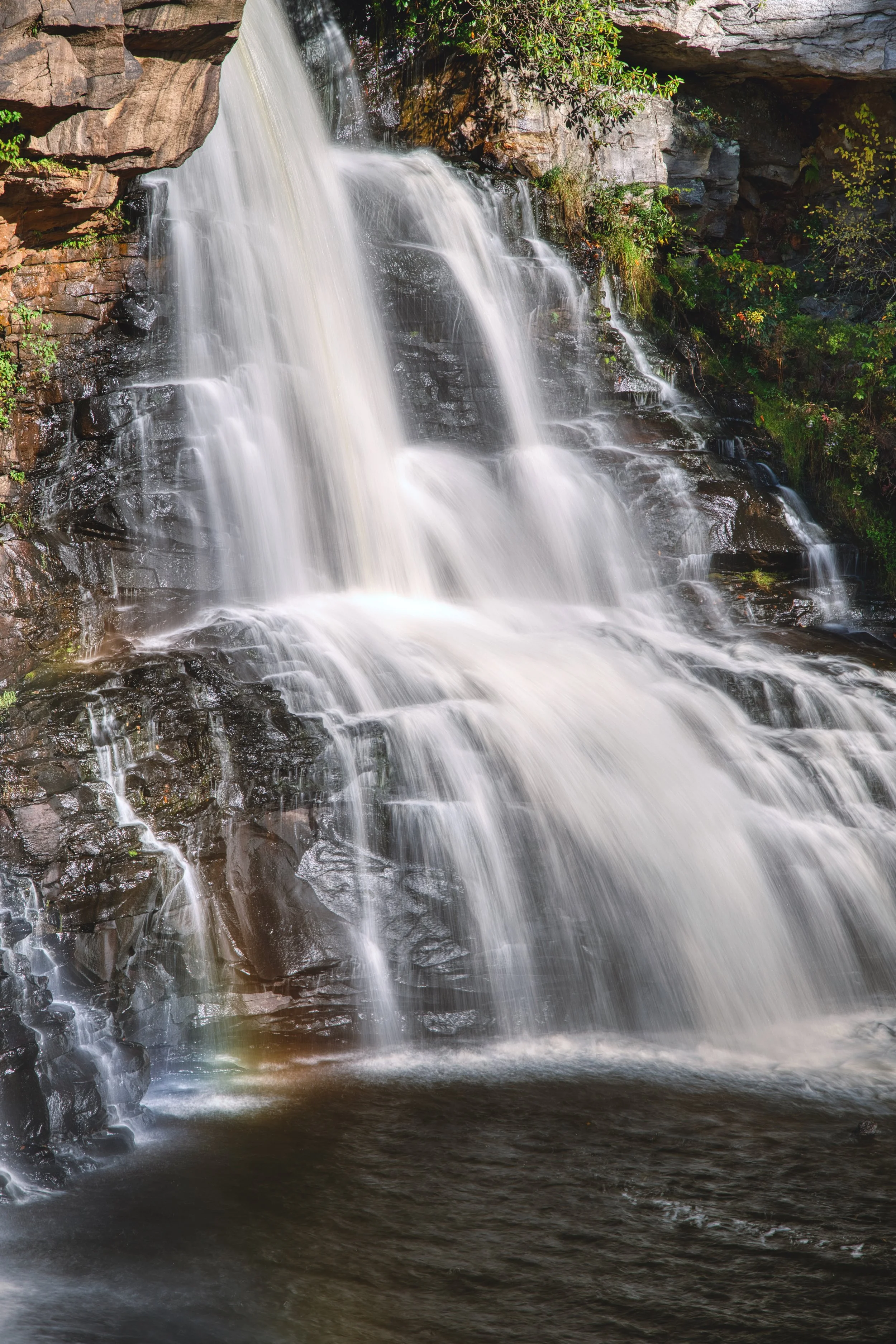 A cascading waterfall flowing over rocks in a forested area.