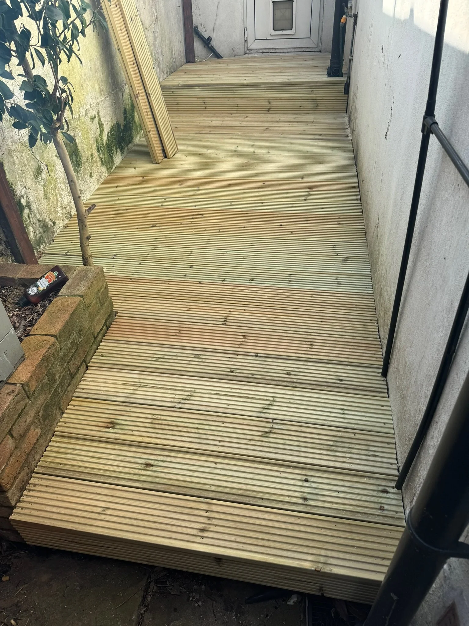 New wooden deck in progress on a small outdoor space with concrete walls and a metal railing.