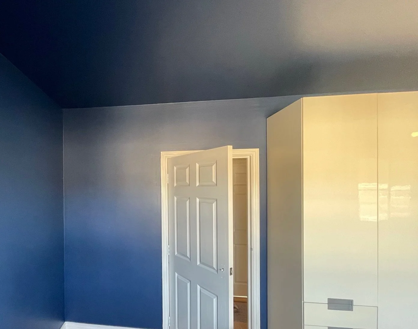 A partially open white door in a blue-walled room with a white cabinet or wardrobe.