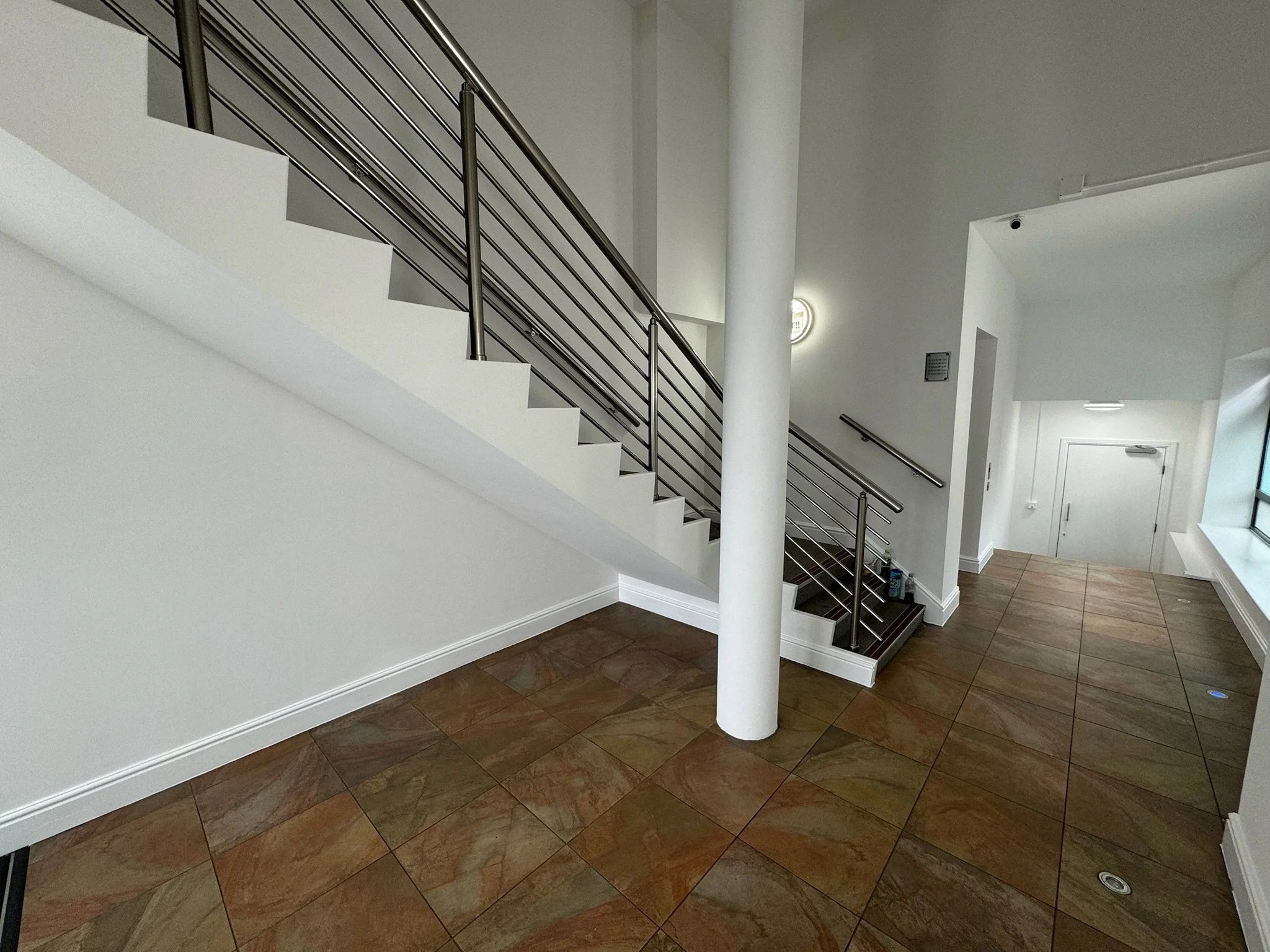 Interior of a modern building with a staircase, tiled floor, white walls, and large window.