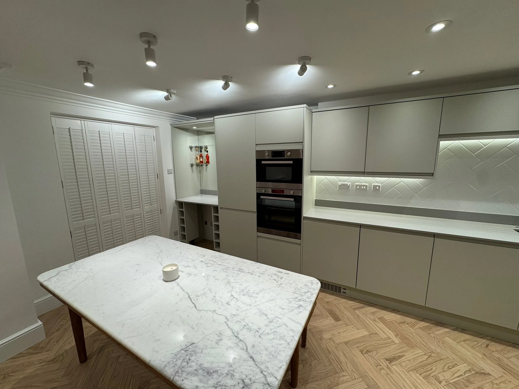 Modern kitchen with white cabinets, marble countertop table, built-in oven, and wood flooring.