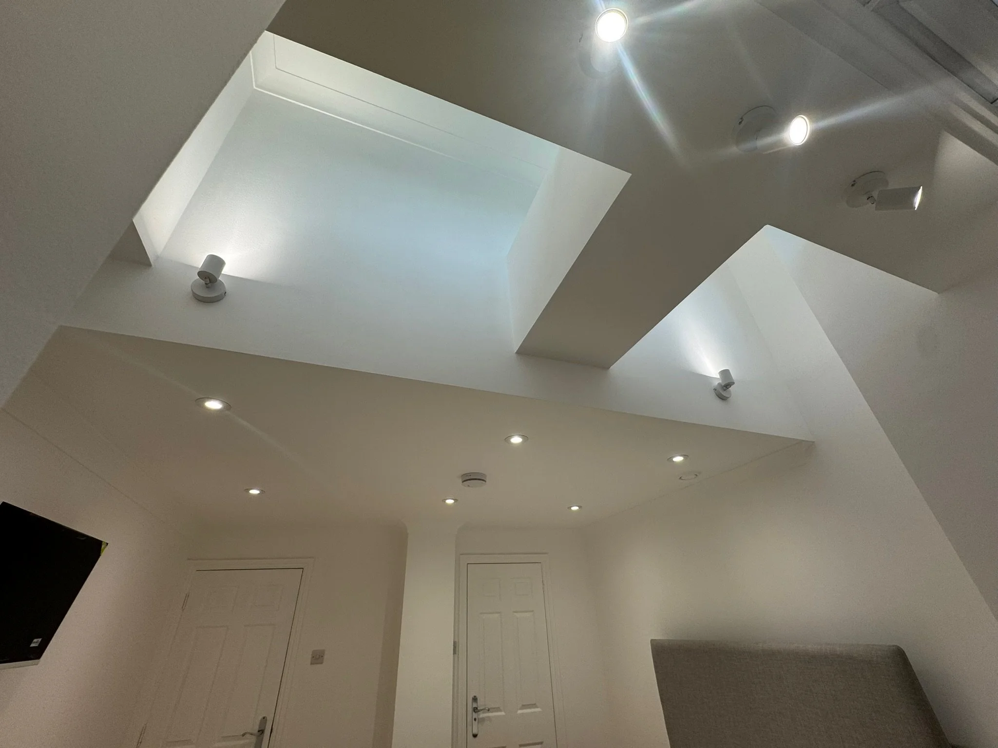Interior view of a modern room with a skylight, recessed lighting, and ceiling spotlights, with a closed door and an upholstered headboard.