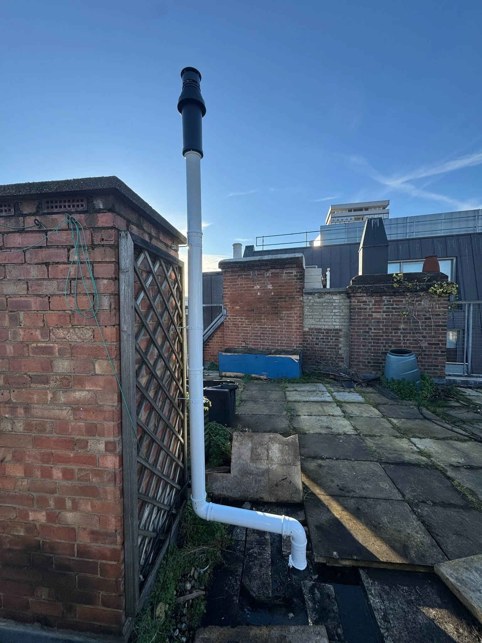 Rooftop with brick and metal walls, a white drain pipe, and a blue sky.