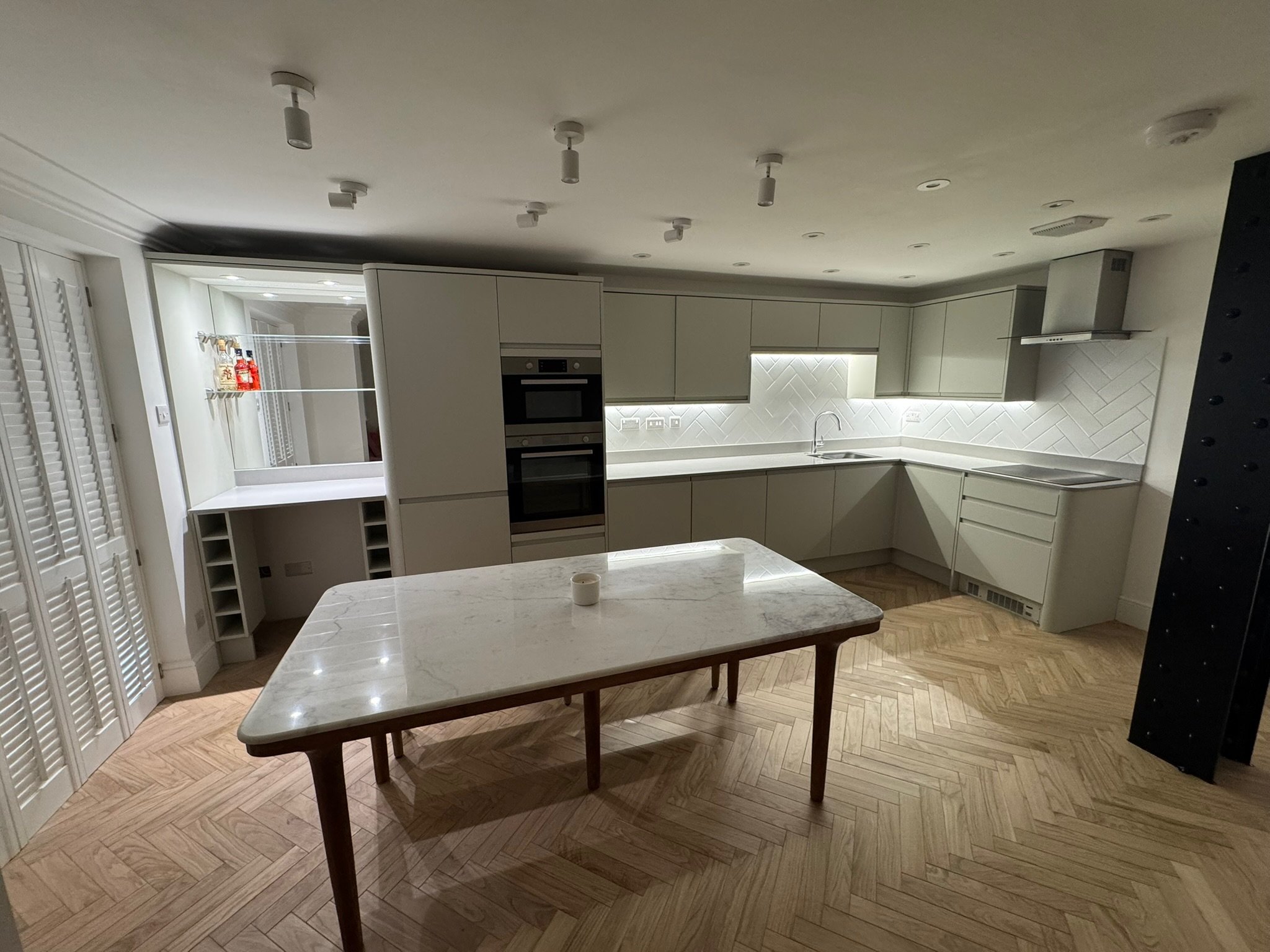 Modern, minimalist kitchen with beige cabinets, marble island, white backsplash, hardwood floor, and various built-in appliances.