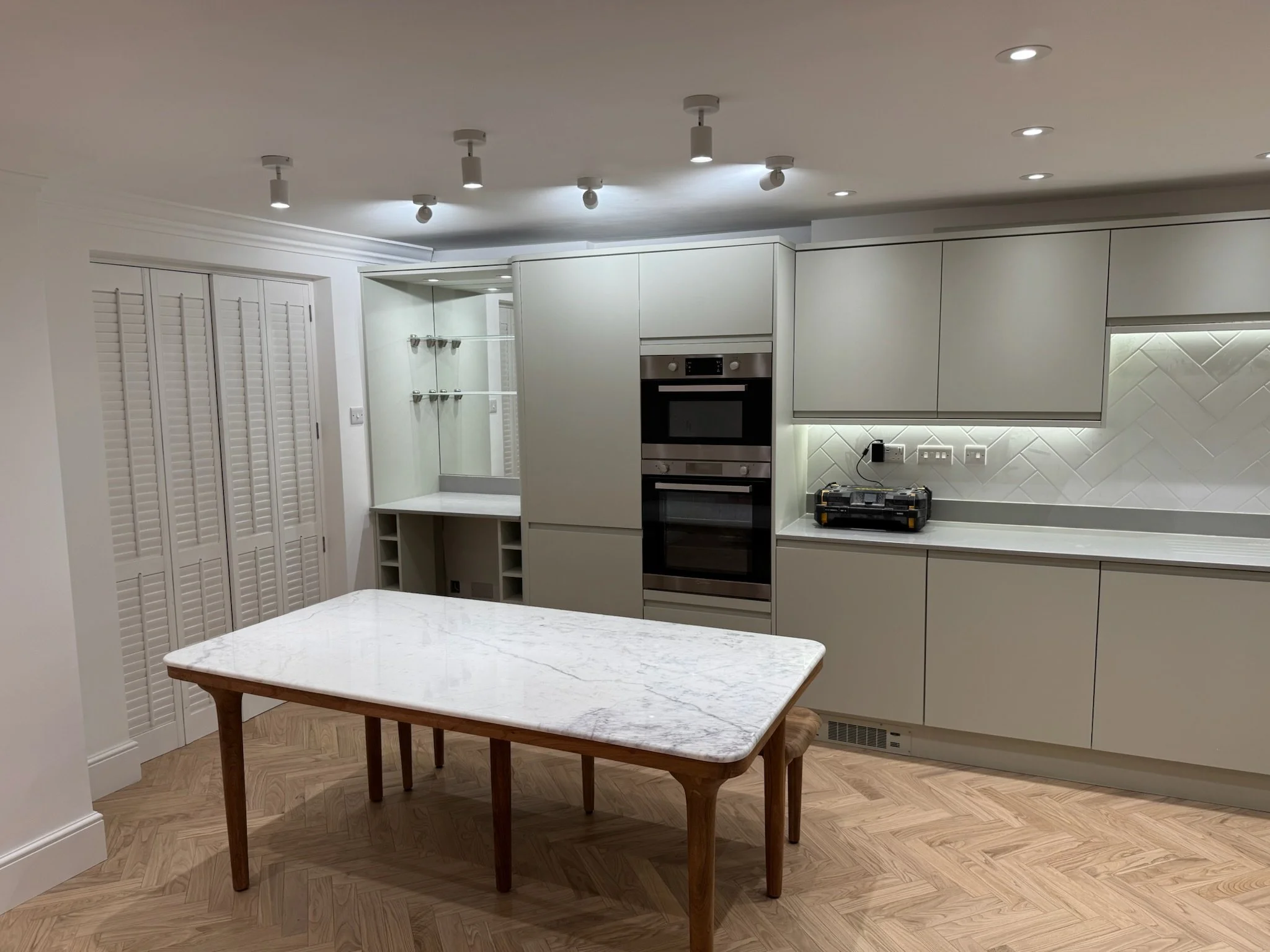 Modern kitchen with white cabinets, built-in oven and microwave, marble-topped island, and wood flooring.