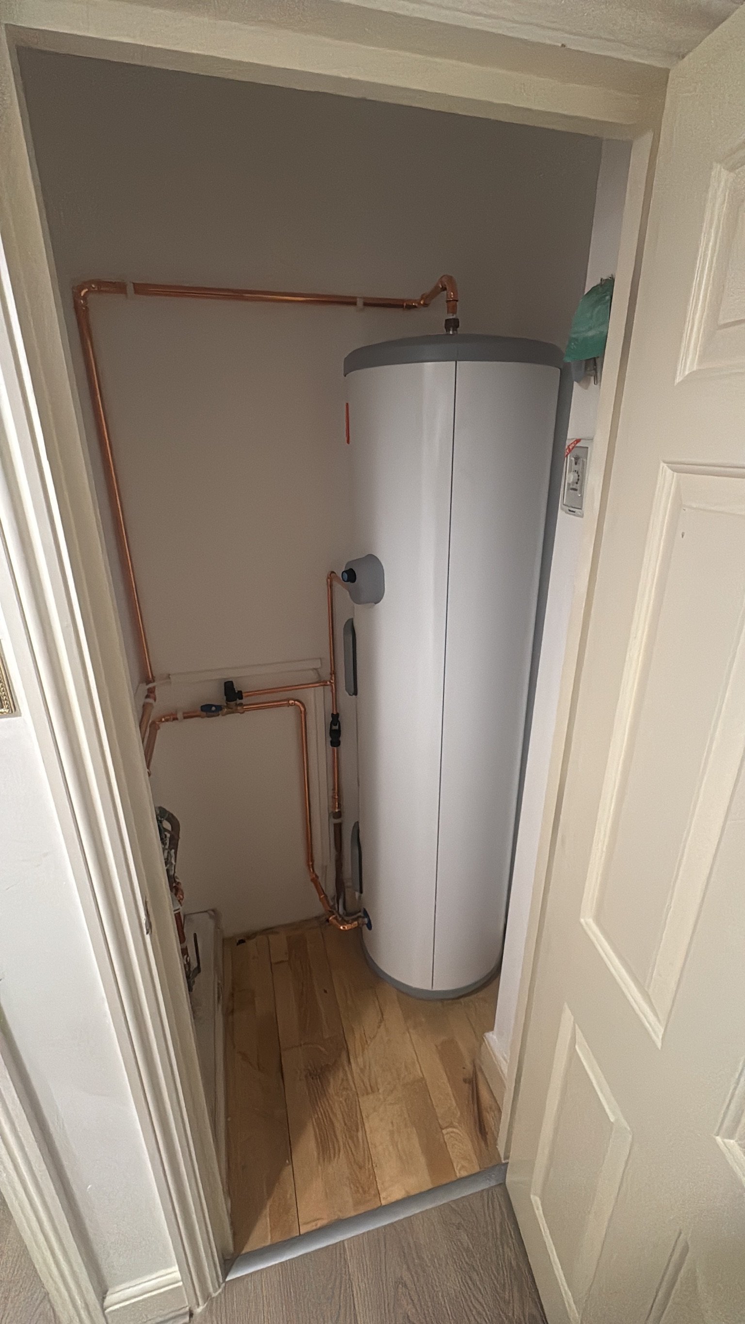 A water heater tank with copper pipes in a small utility closet.