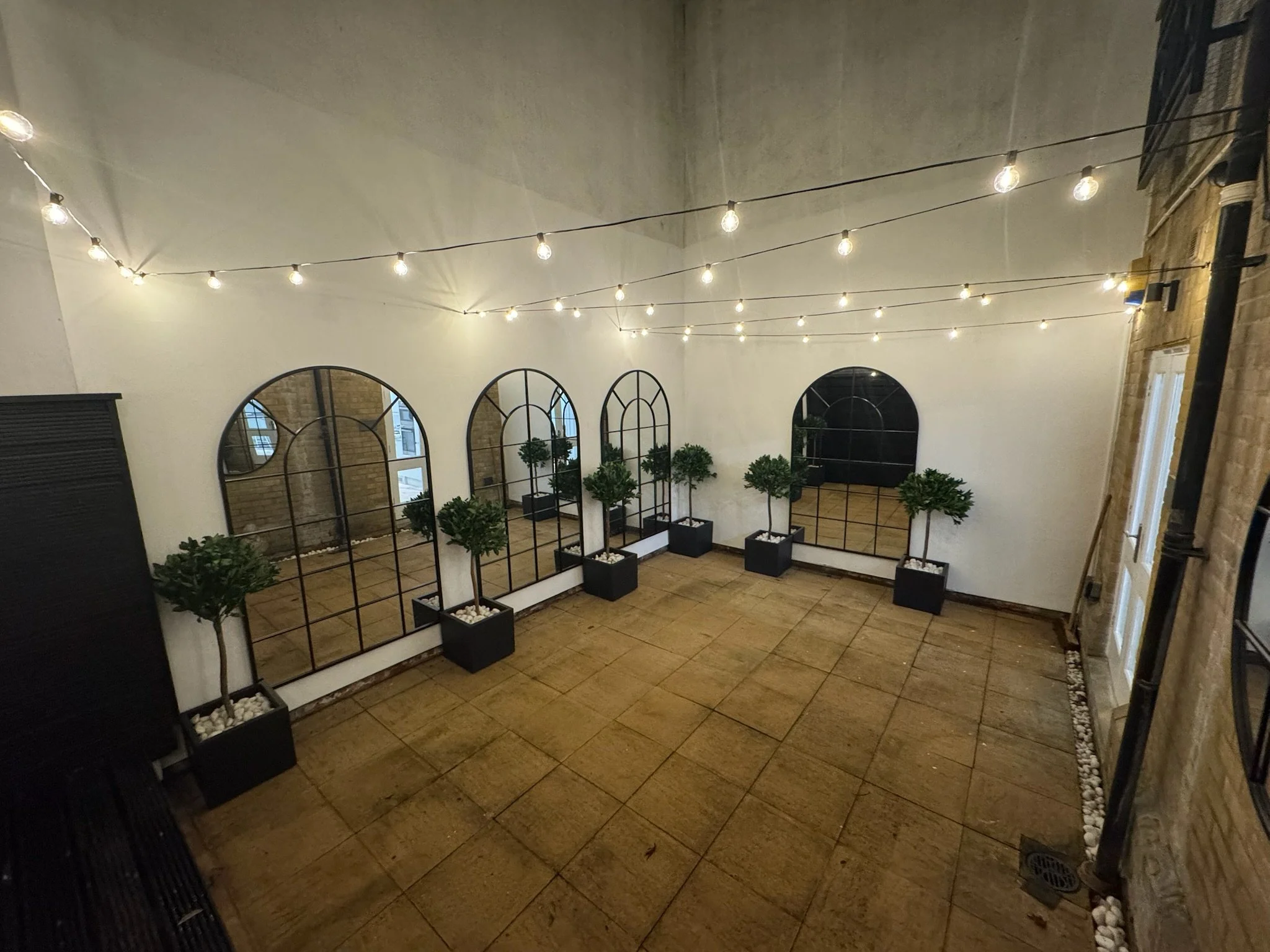 Interior of a rooftop patio with string lights, large mirrors on the wall, and potted trees.