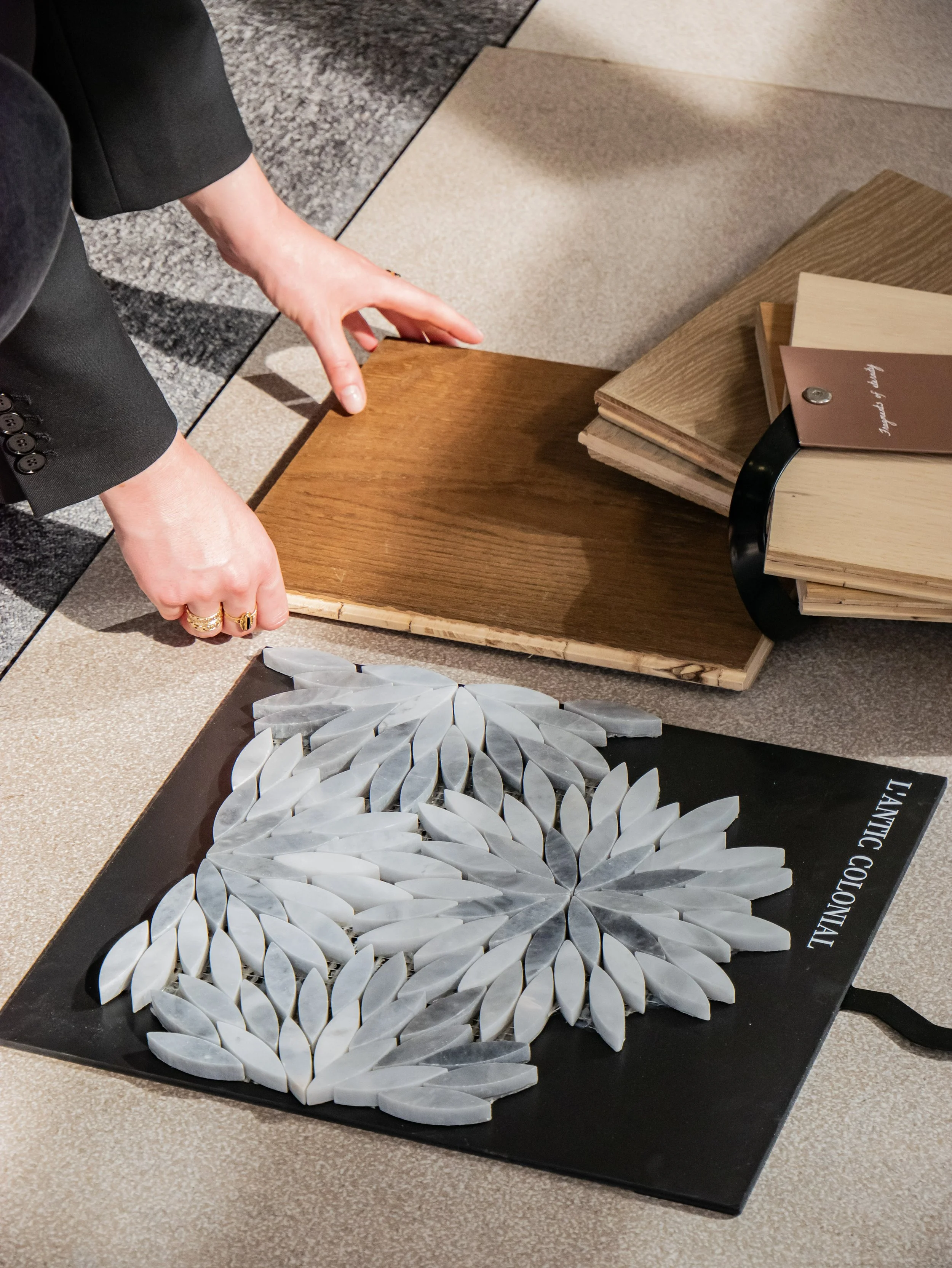 Une personne en costume noir manipule une œuvre d'art composée de feuilles de pierre blanche disposées en forme de lion sur un socle noir, avec des livres de couleurs variées à côté.