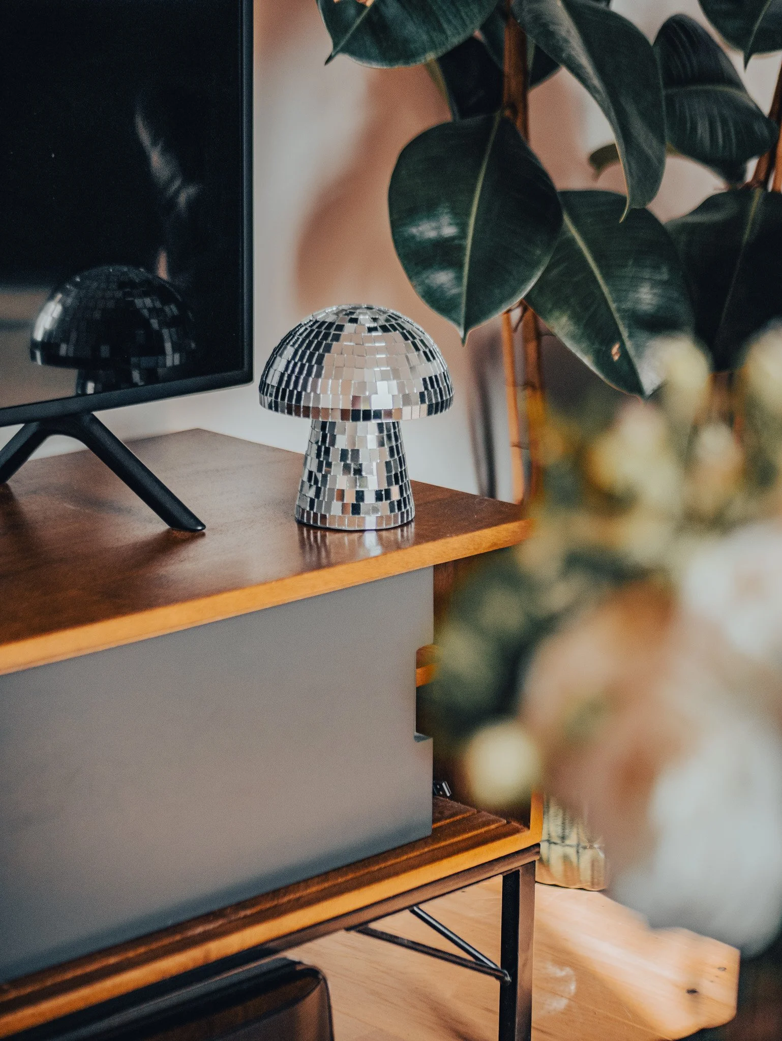 Une lampe en miroir disco sur une étagère en bois, à côté d'un moniteur et d'une plante verte