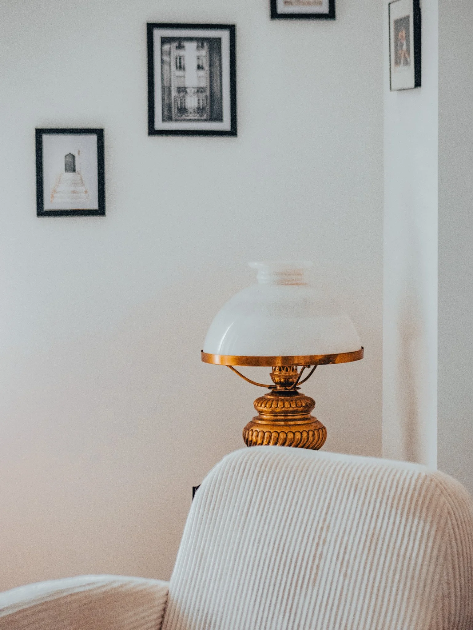Lampe de table vintage avec base en or et abat-jour blanc, placée derrière un fauteuil beige à rayures.