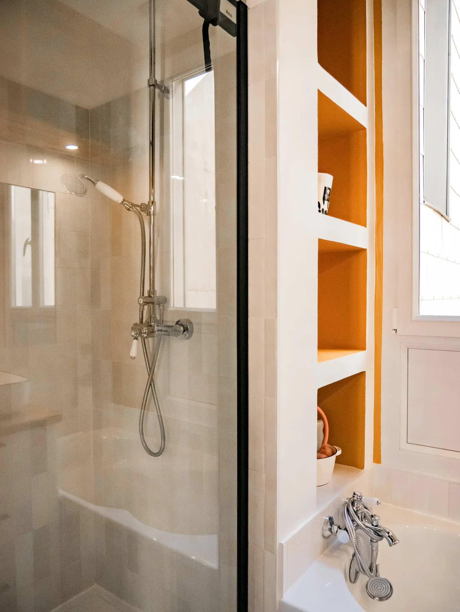 Rénovation d'un salle de bain dans un appartement ancien à Rouen. Meubles sur-mesure avec étagères et placards en bois foncé, douche à l'italienne et baignoire avec huisseries noires, peinture couleur cumin, miroir sur mesure avec zellige mural blanc