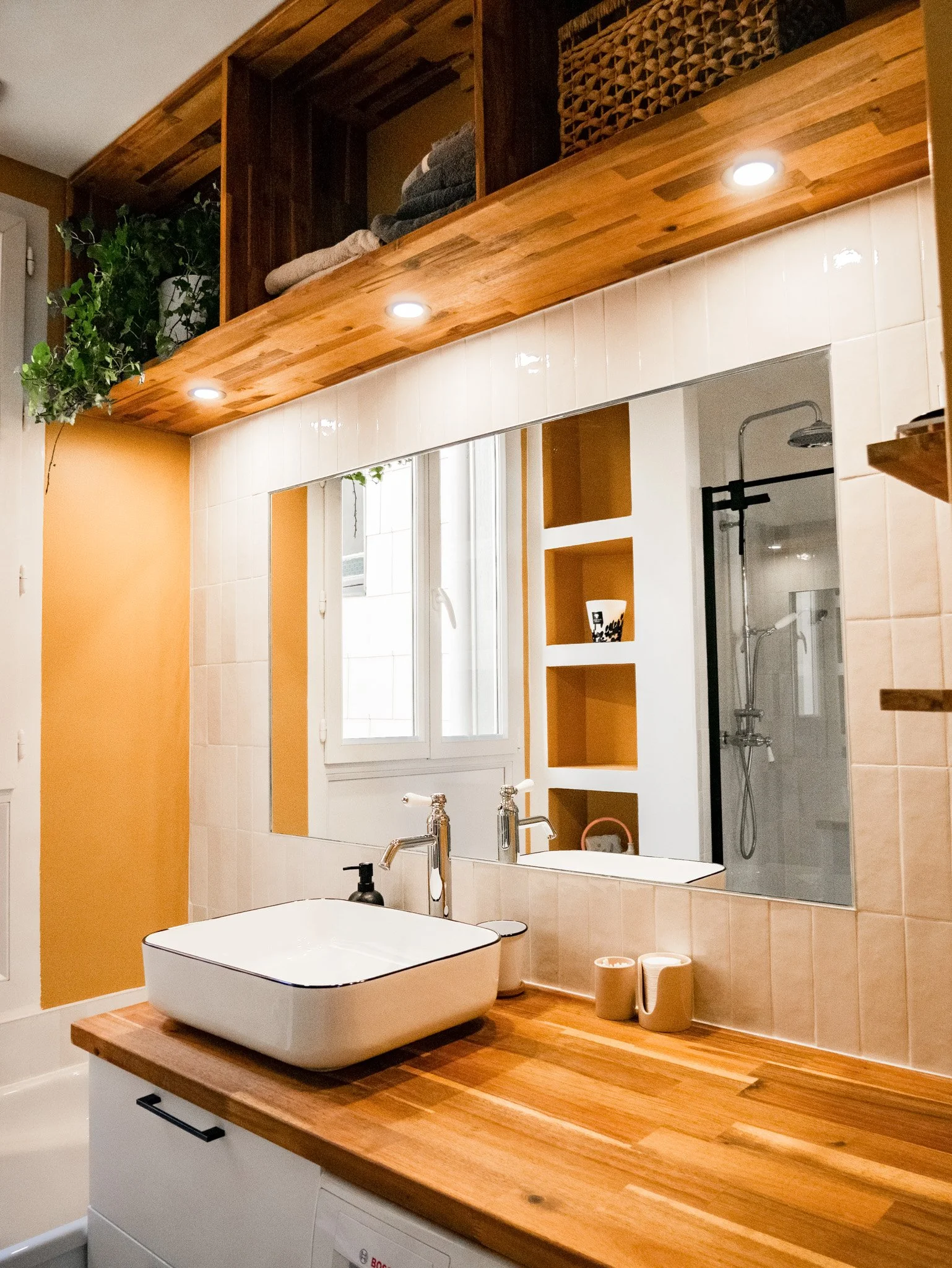 Rénovation d'un salle de bain dans un appartement ancien à Rouen. Meubles sur-mesure avec étagères et placards en bois foncé, douche à l'italienne et baignoire avec huisseries noires, peinture couleur cumin, miroir sur mesure avec zellige mural blanc