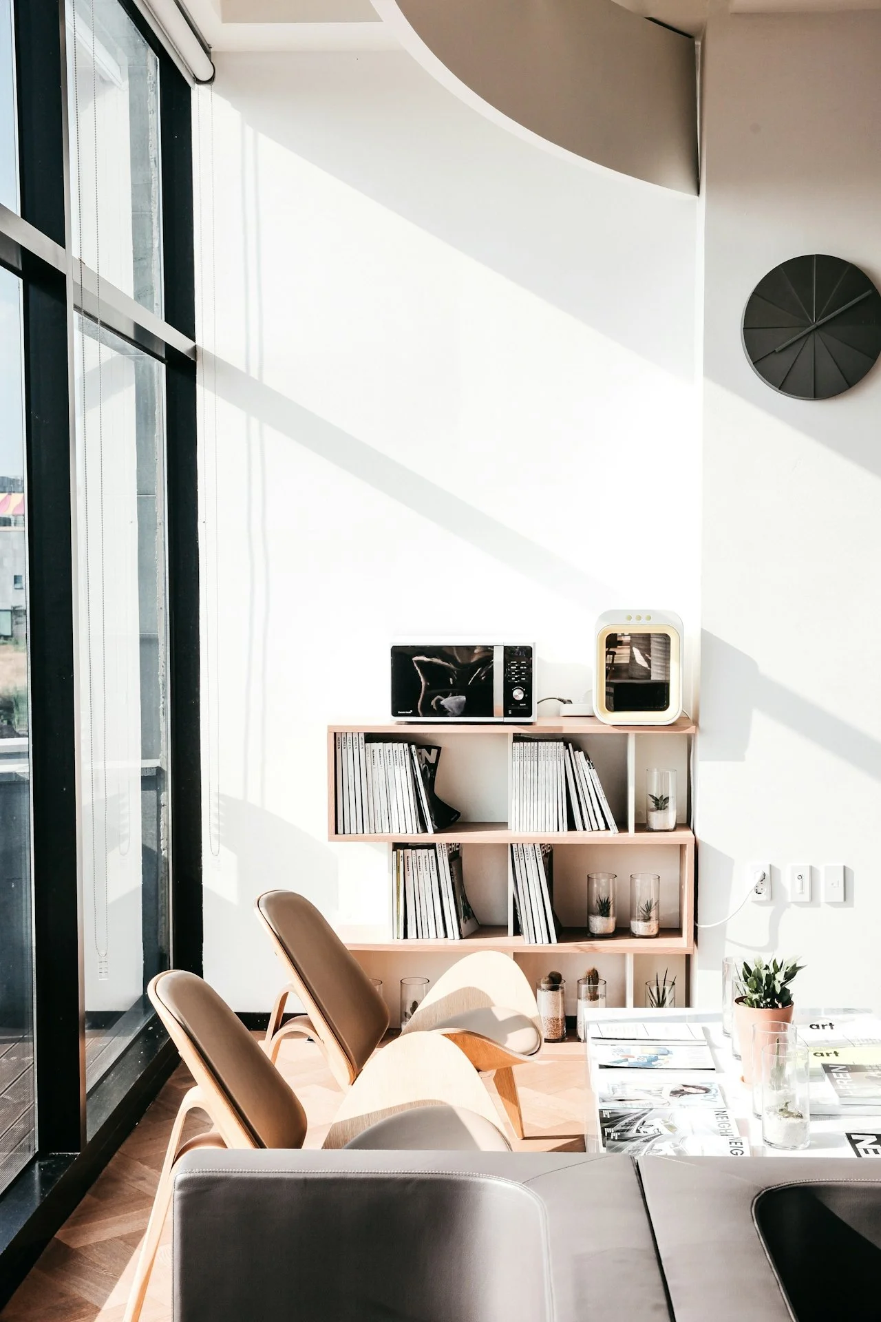 Modern dining area with a table, chairs, a bookshelf, and large windows letting in sunlight.