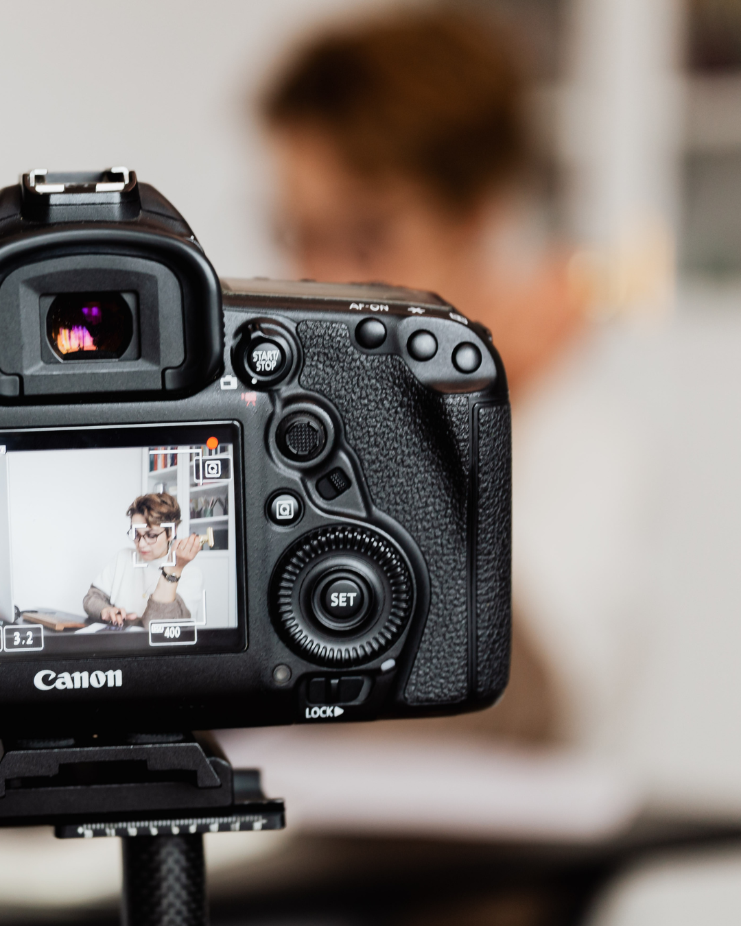 Câmera Canon tirando foto de uma pessoa desfocada ao fundo.