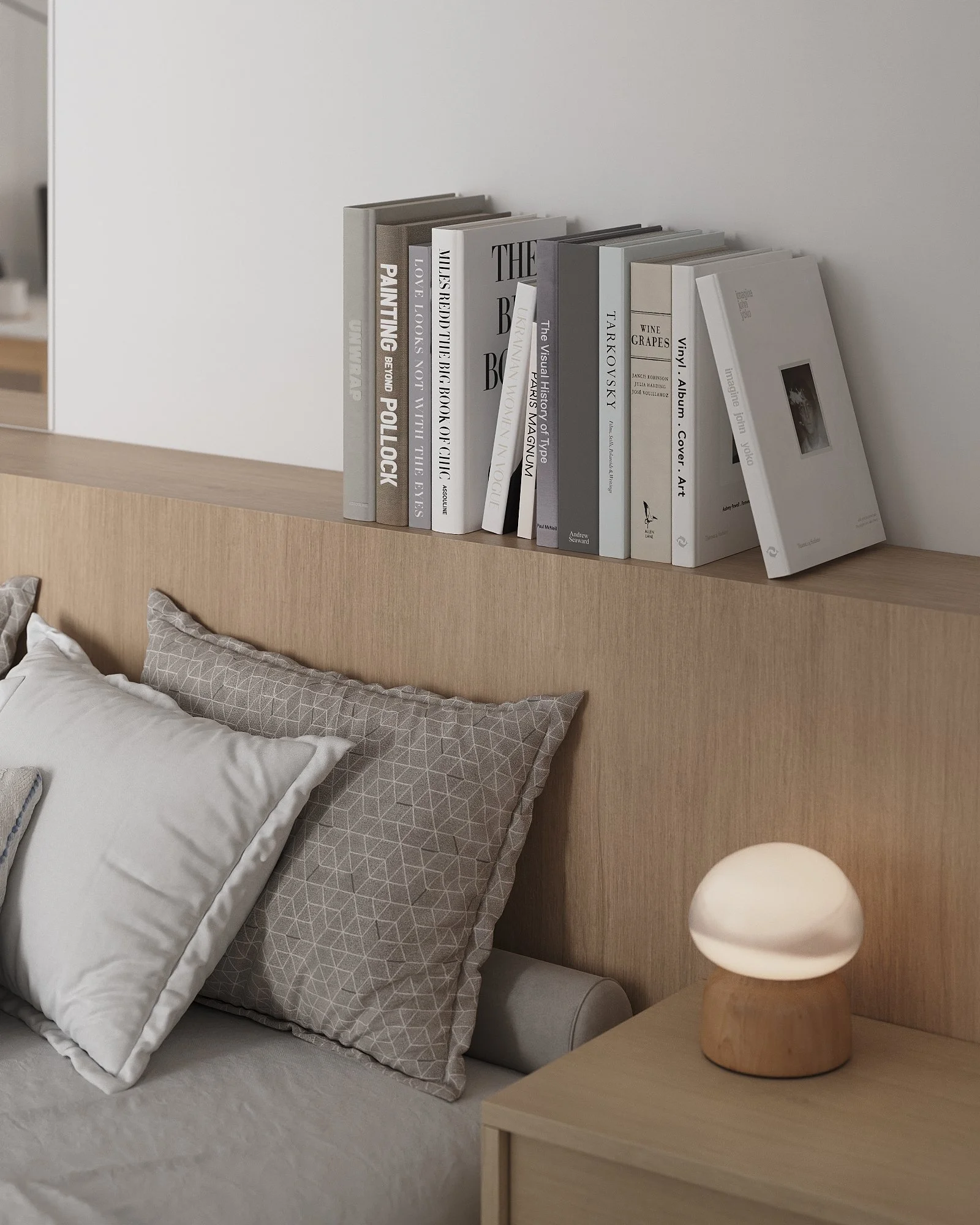Books on a wooden headboard shelf above a bed with beige and white pillows, and a small lamp on a bedside table.