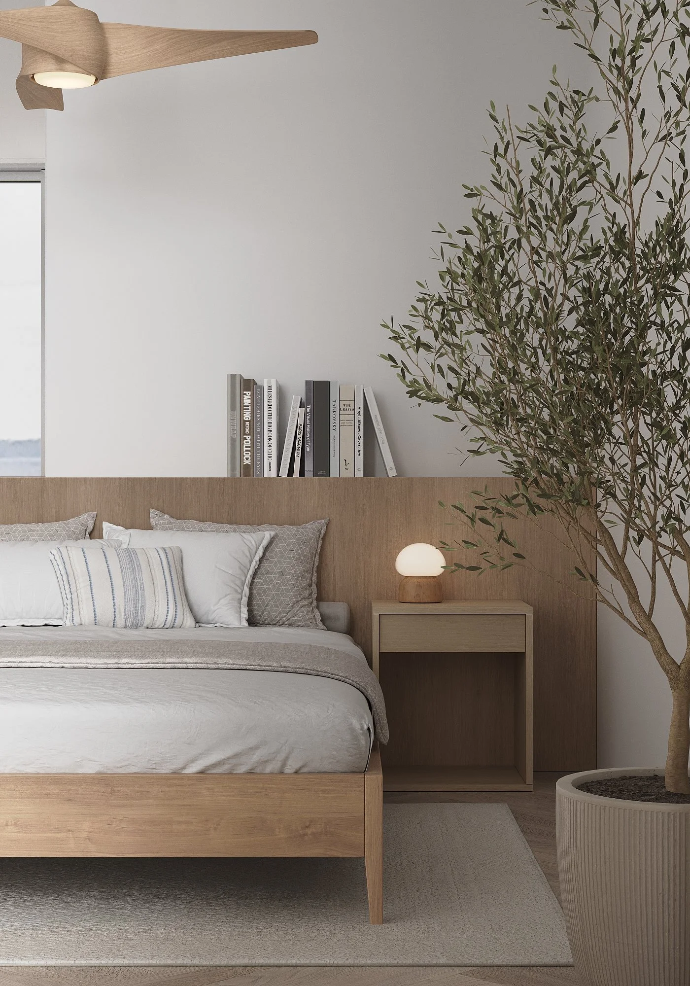 A minimalist bedroom with a wooden bed, layered with white and gray pillows, and a beige bedspread. A light-colored nightstand with a modern table lamp is beside the bed. A large potted plant with green leaves is on the right, and a shelf with books 