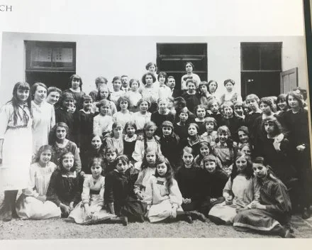 Groep kinderen en volwassenen poseert buiten voor een schoolgebouw.
