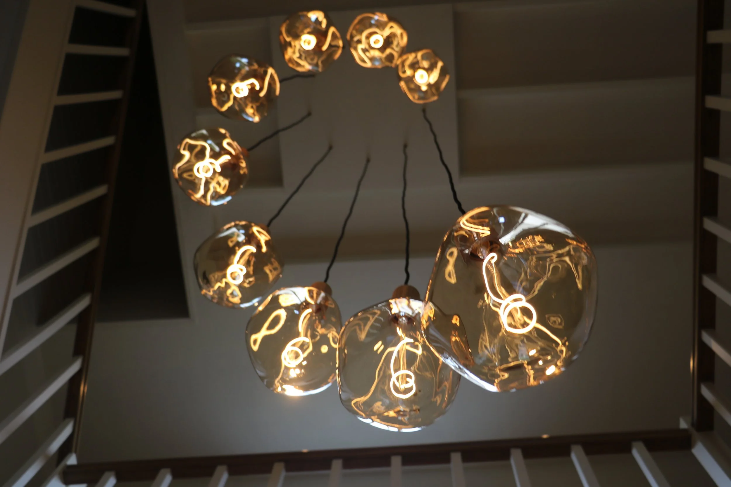Hanglamp met glazen bollen en gloeilampen, bekeken vanaf beneden, met trapleuning aan zijkant.