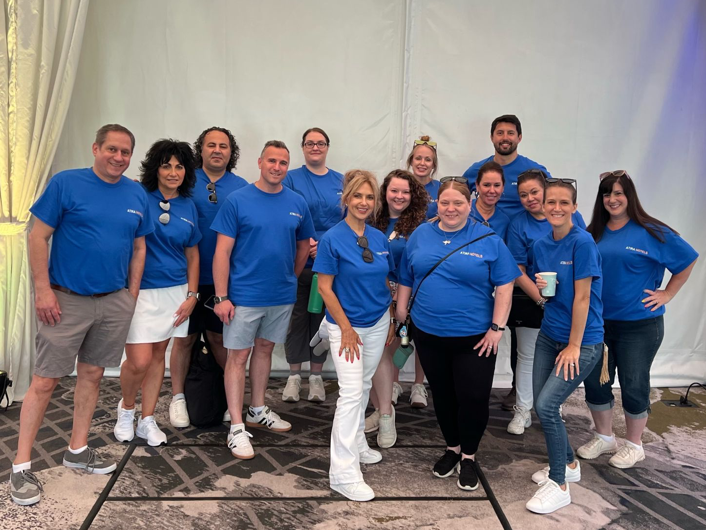 Group of people in blue shirts posing together indoors at a conference or event.