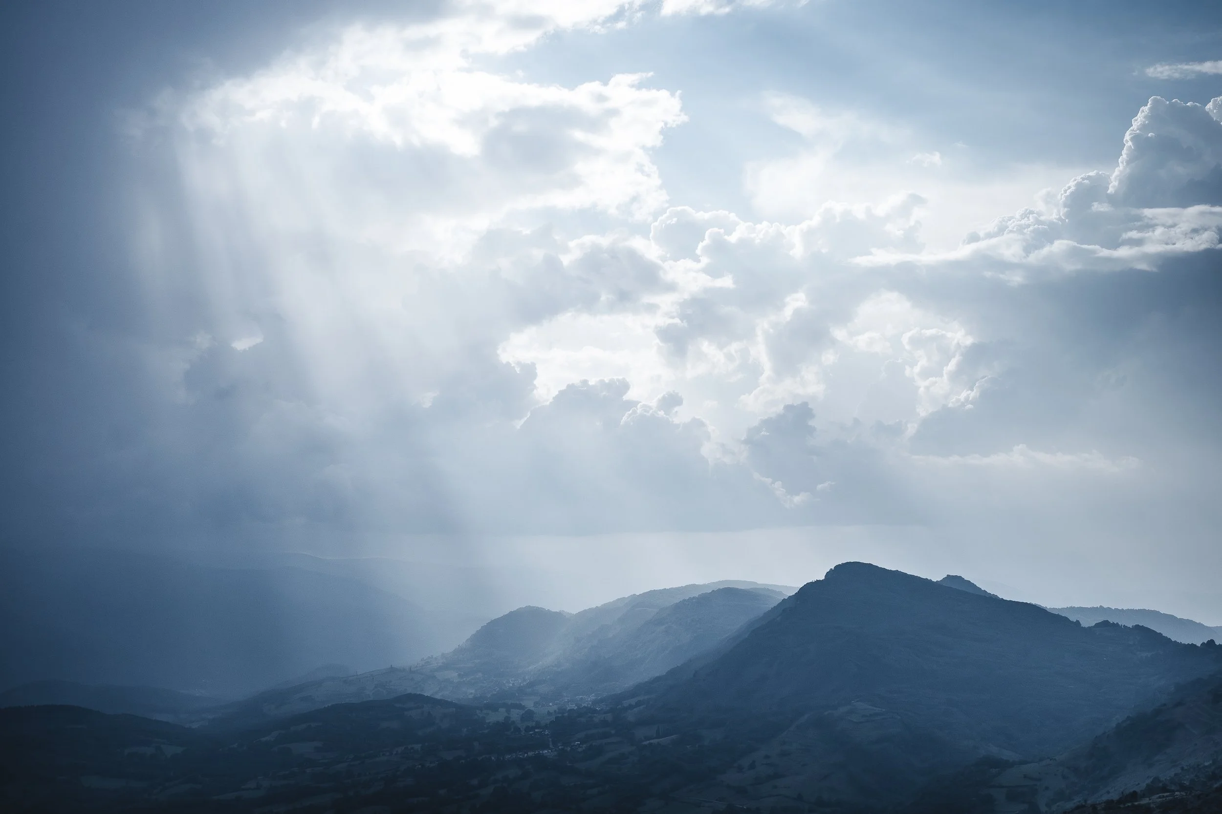 Paysage de montagnes sous un ciel nuageux avec rayons de soleil perçant à travers les nuages.