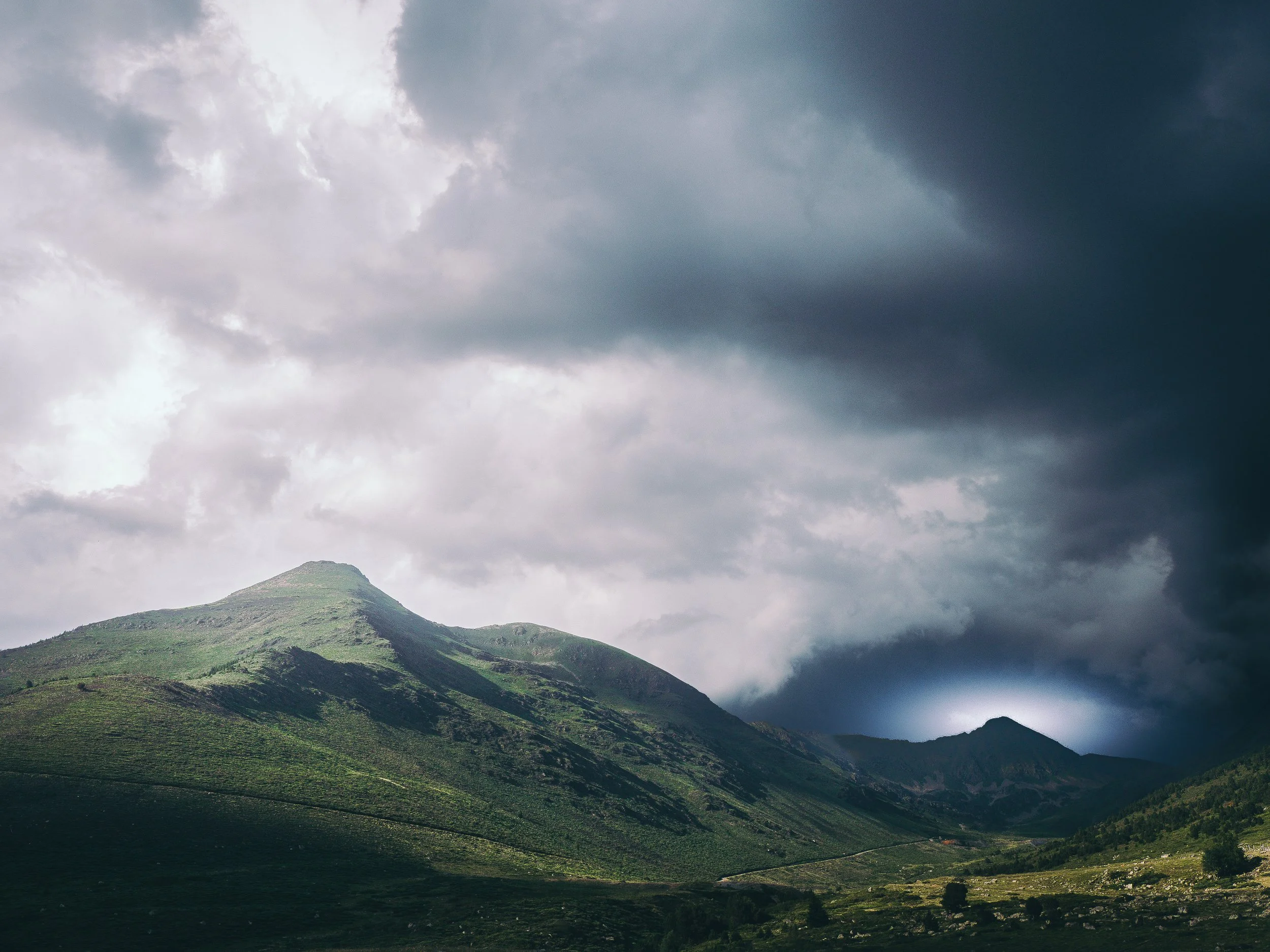 Montagnes verdoyantes sous un ciel orageux avec des nuages sombres.