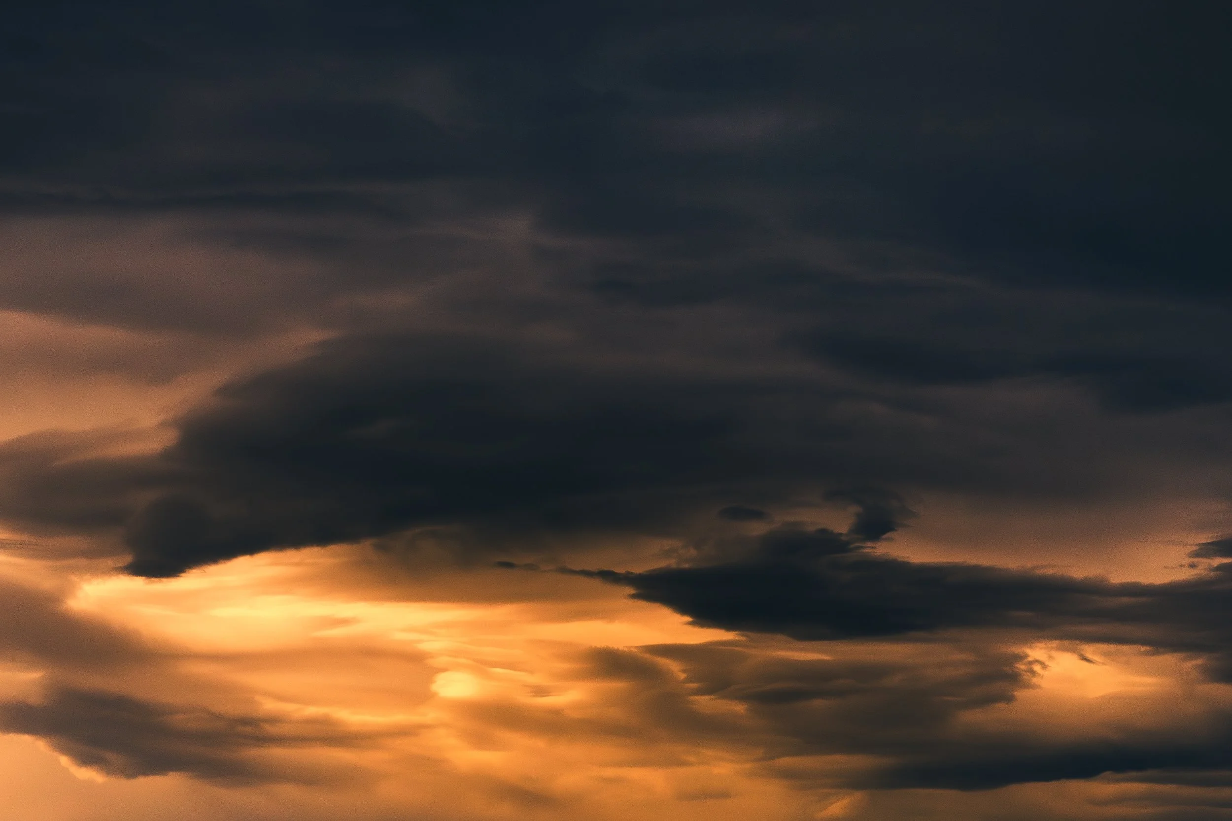 Ciel nuageux avec des couleurs d'orange et de gris lors du coucher du soleil.