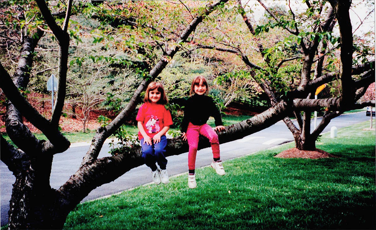 Childhood photo of Jess and her friend Suzy sitting together on a tree branch