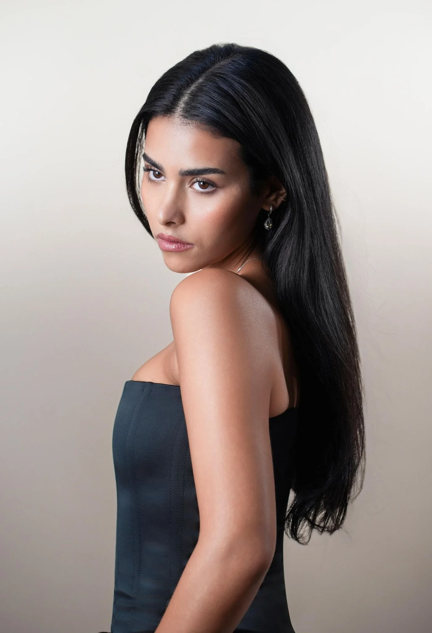 Woman with long black hair, wearing a black top and a necklace, looking directly at the camera.