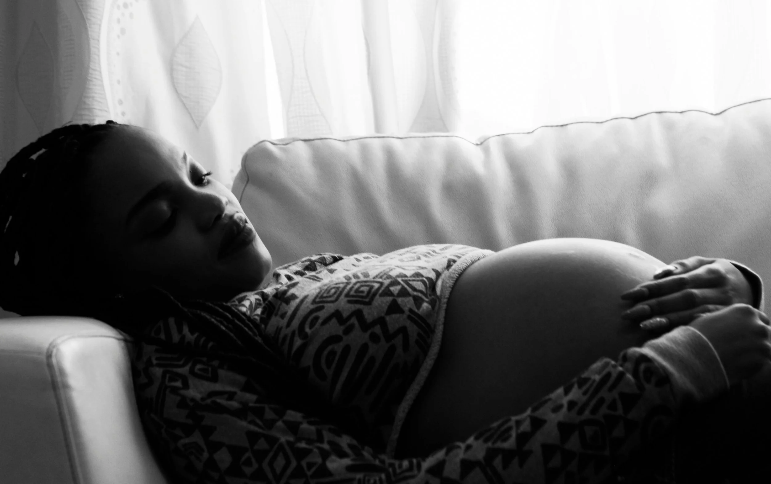 Pregnant woman resting peacefully with eyes closed on a couch, practicing deep relaxation as part of self-hypnosis in Hypnobirthing