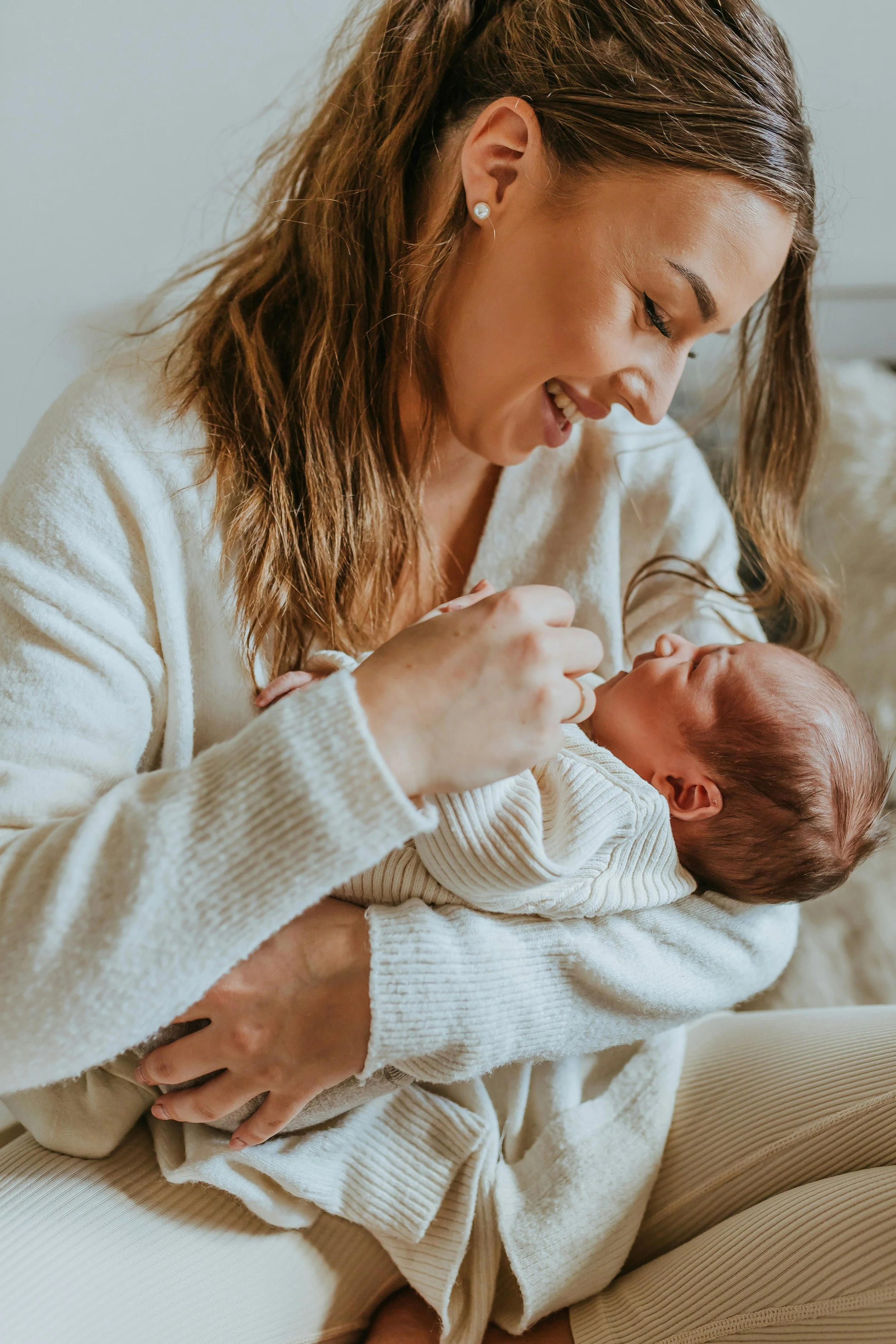 New mother tenderly holding her newborn by a sunlit window, postpartum support from Birthing by Nature in Simi Valley, CA