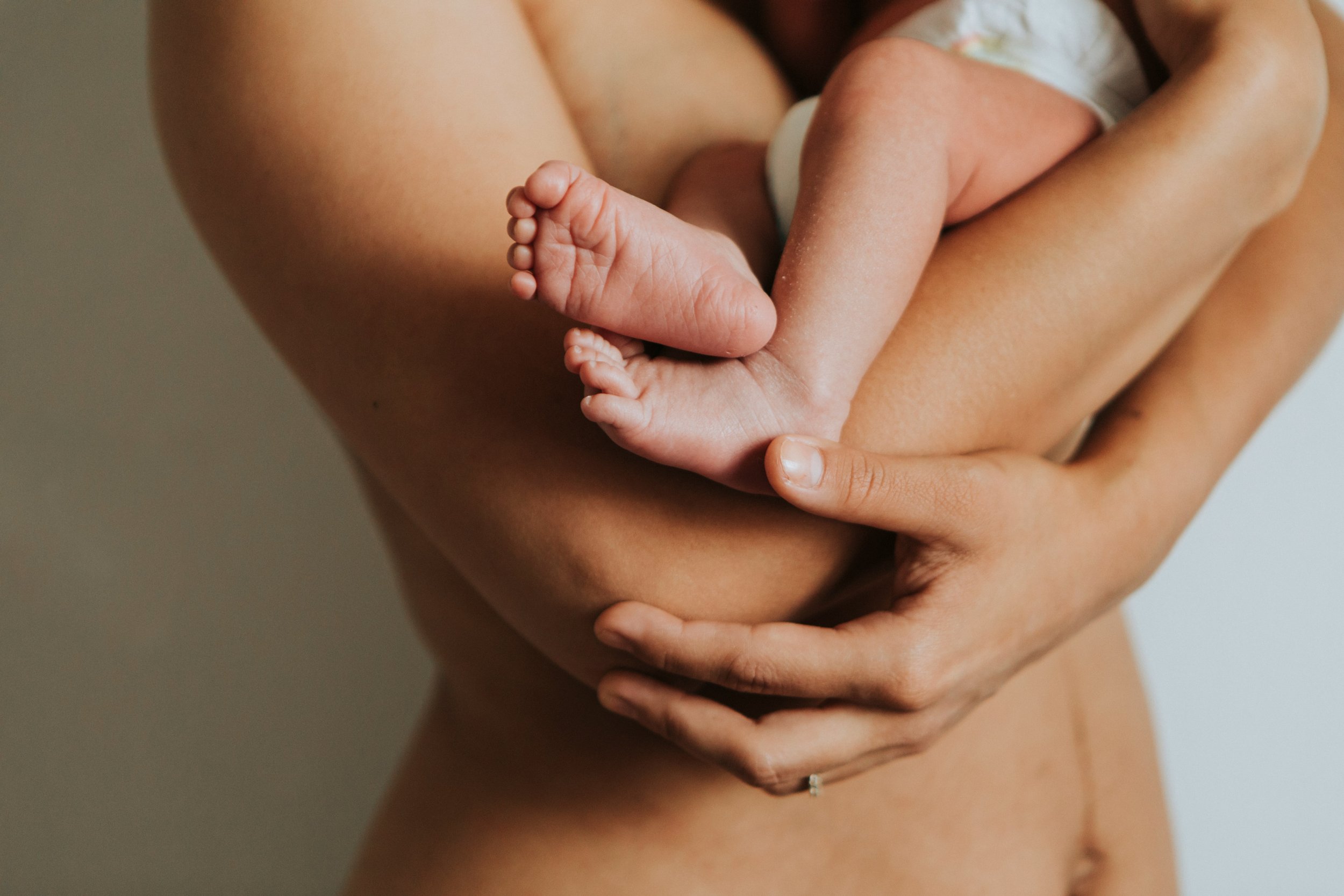 Postpartum mother gently holding her newborn's feet, calm birth recovery with Birthing by Nature