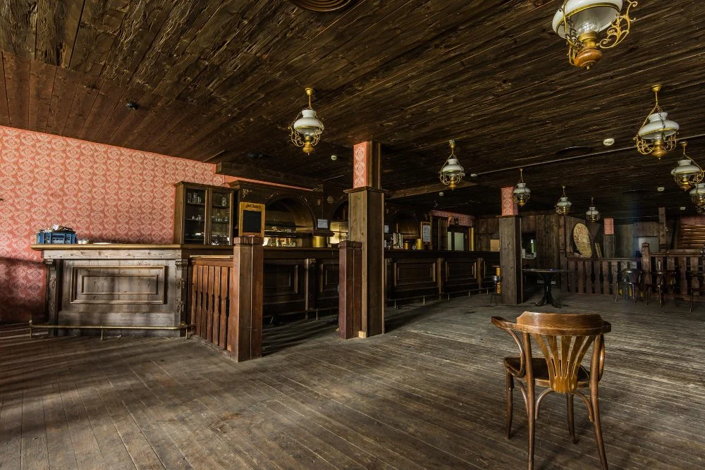 Empty vintage-style bar with wooden counters, chairs, and dim lighting.