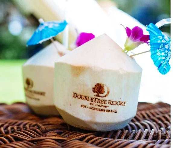 Eco-friendly branded coconut drinks with umbrellas and flowers on a woven surface, branded with the Doubletree Resort logo.