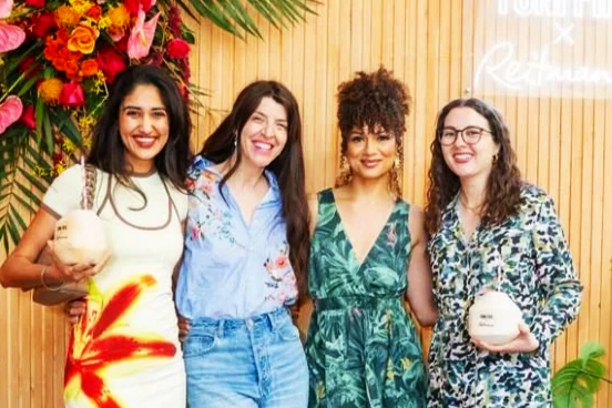 Four women smiling and posing together at an event, with holding custom branded coconuts