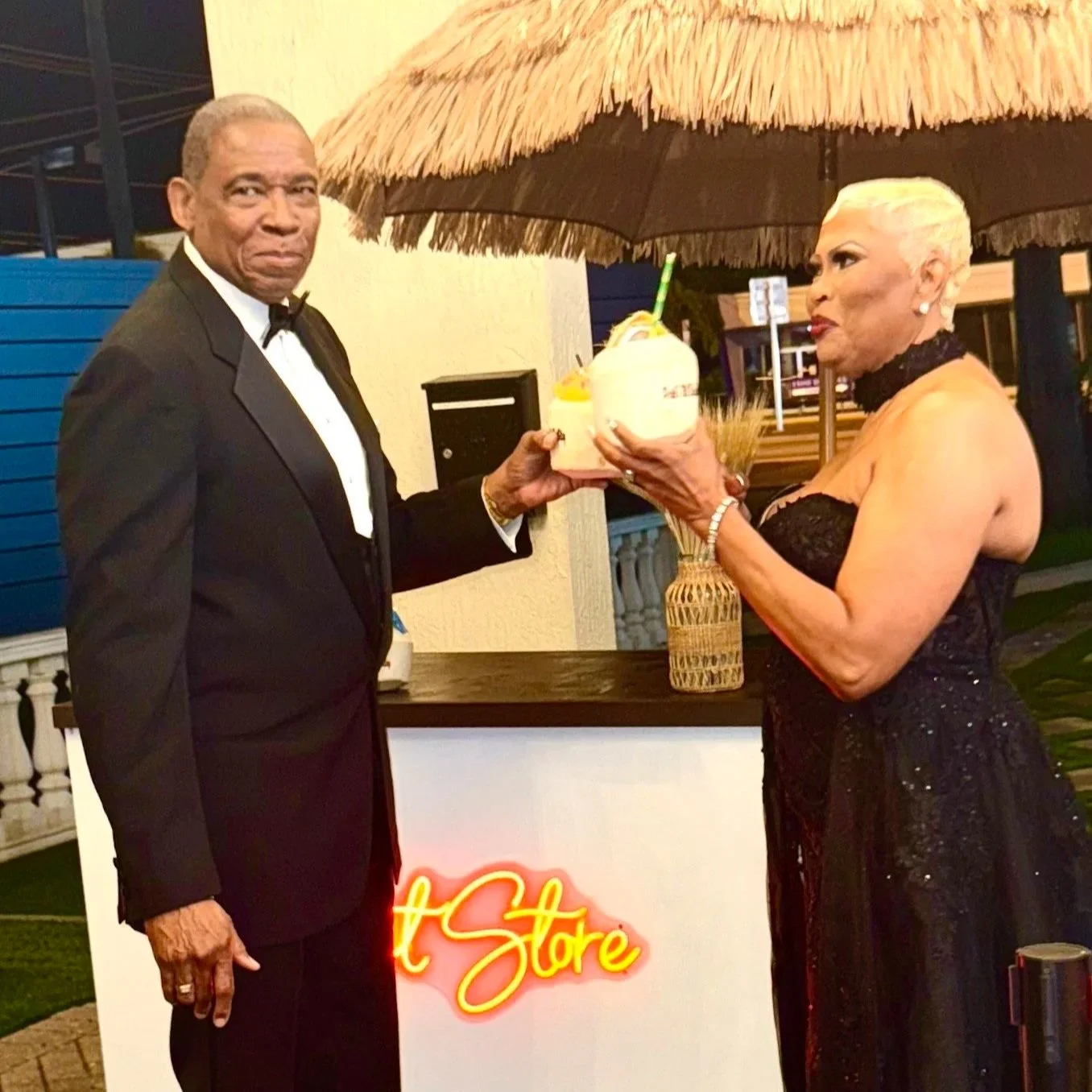 An elderly man presents a custom coconut drink to an elderly woman.