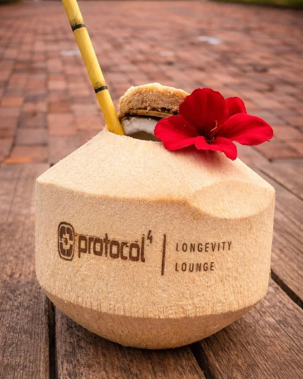A fresh coconut drink with a straw, topped with a red flower and a cookie, placed on a wooden surface.