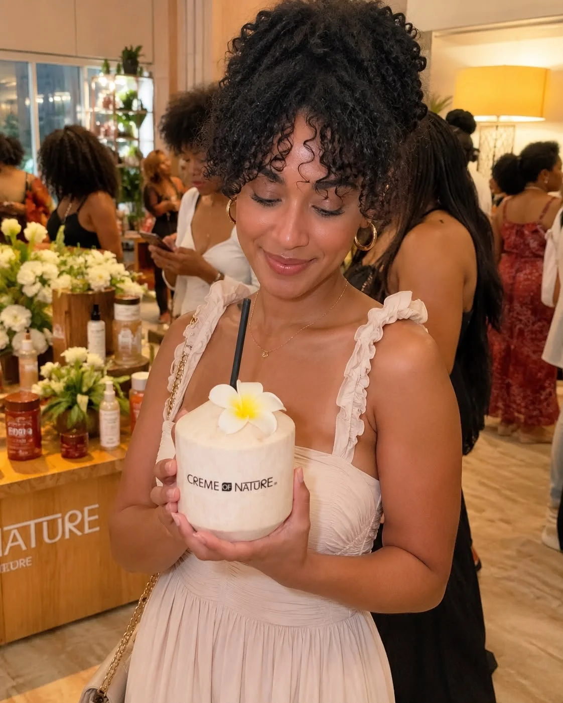 Woman holding a coconut drink with a flower decoration at an indoor event.