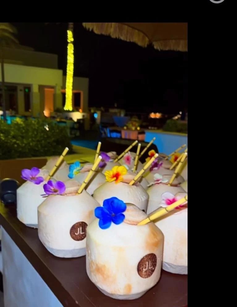 Promotional coconuts with colorful flowers and straws arranged on a table at night.