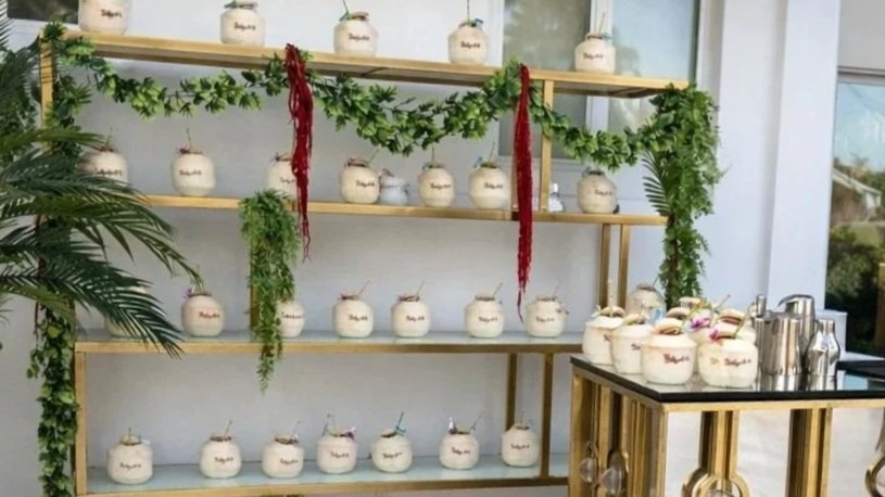 A display of white ceramic jars with bamboo lids on wooden shelves with greenery and red decorative hanging ribbons, located near a window