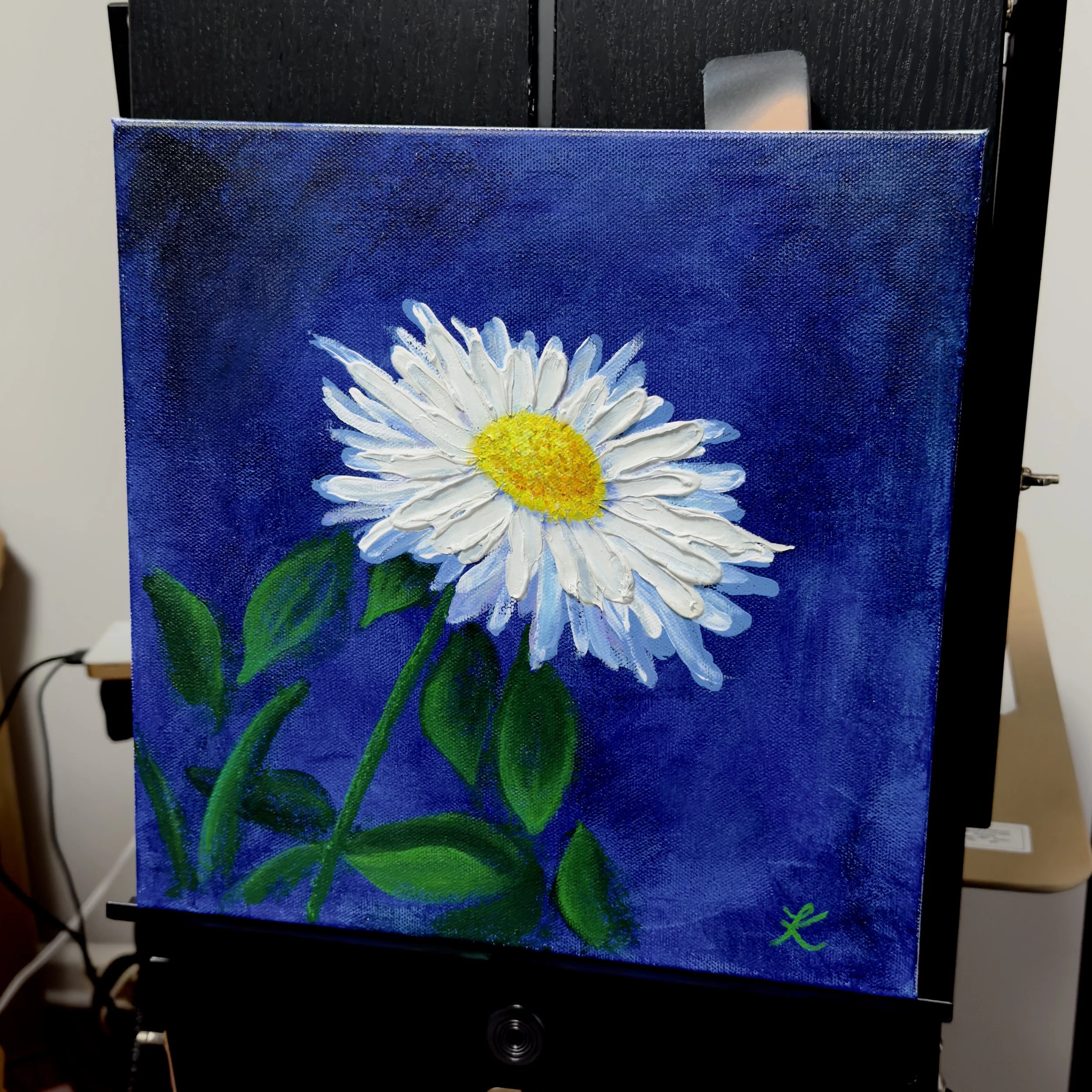 Acrylic painting of single daisy on cobalt blue background, set on an easel