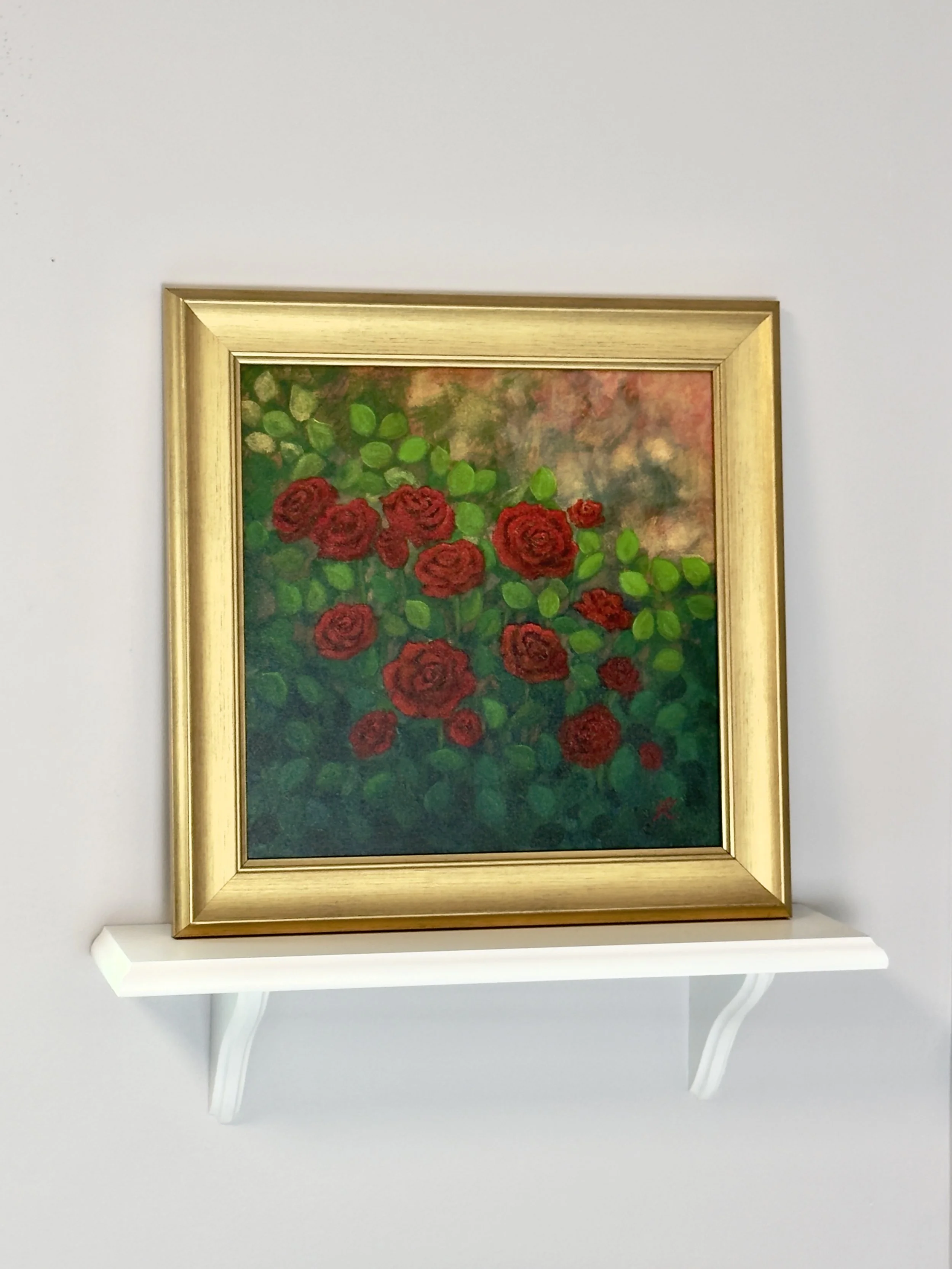 gold framed acrylic painting of red roses set on a wall shelf