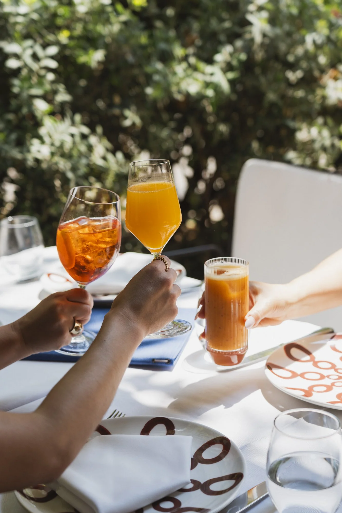 Two takeaway coffee cups with black lids and straws on a round white table next to a person using a laptop. The cups are labeled "crémo Thessaloniki."