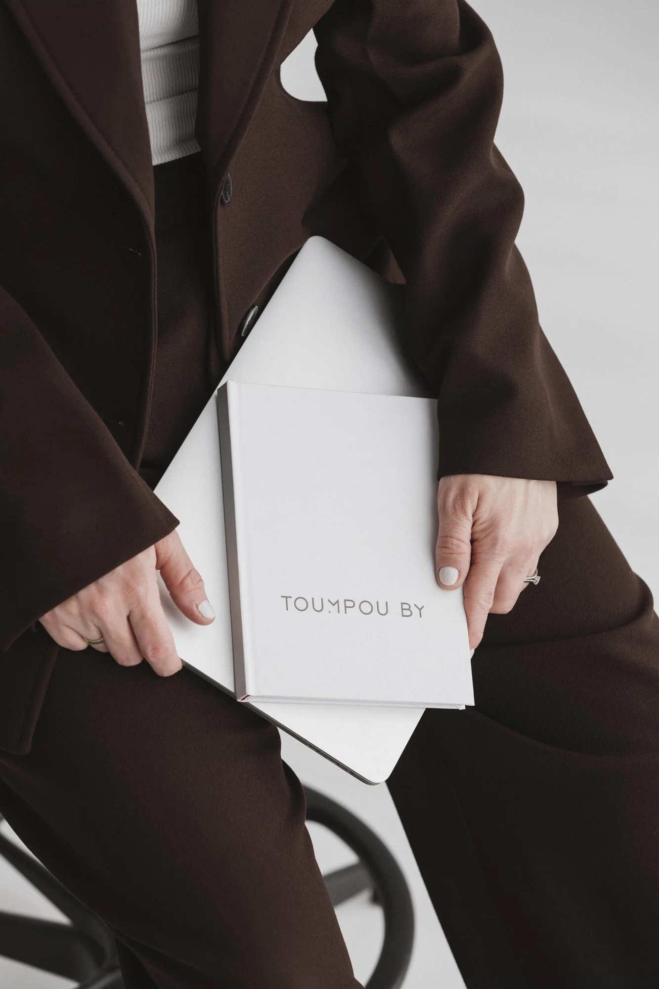 Person in brown suit holding a white book with "TOUMPOU BY" on cover.