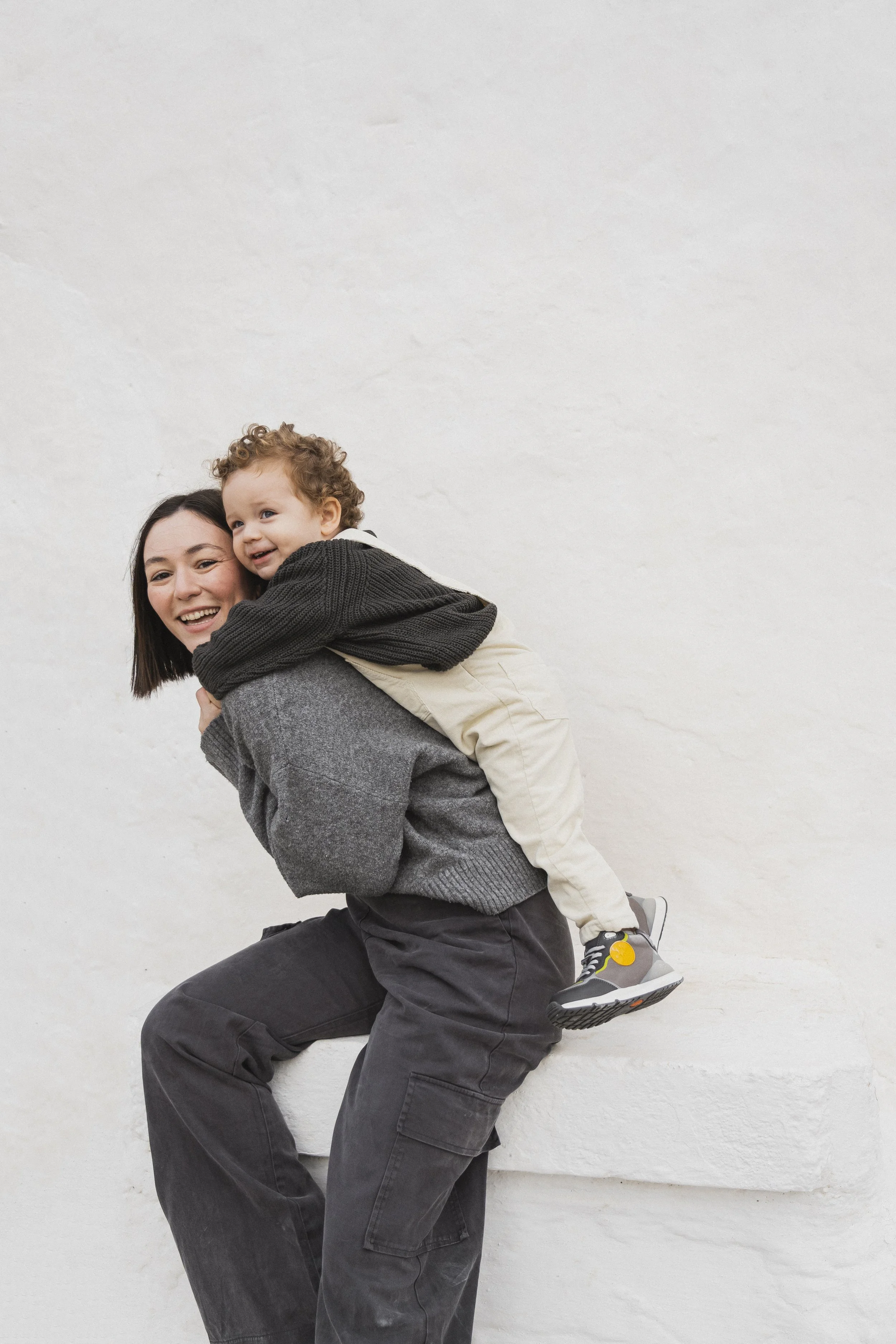 Woman giving child a piggyback ride, both smiling, against a white background.