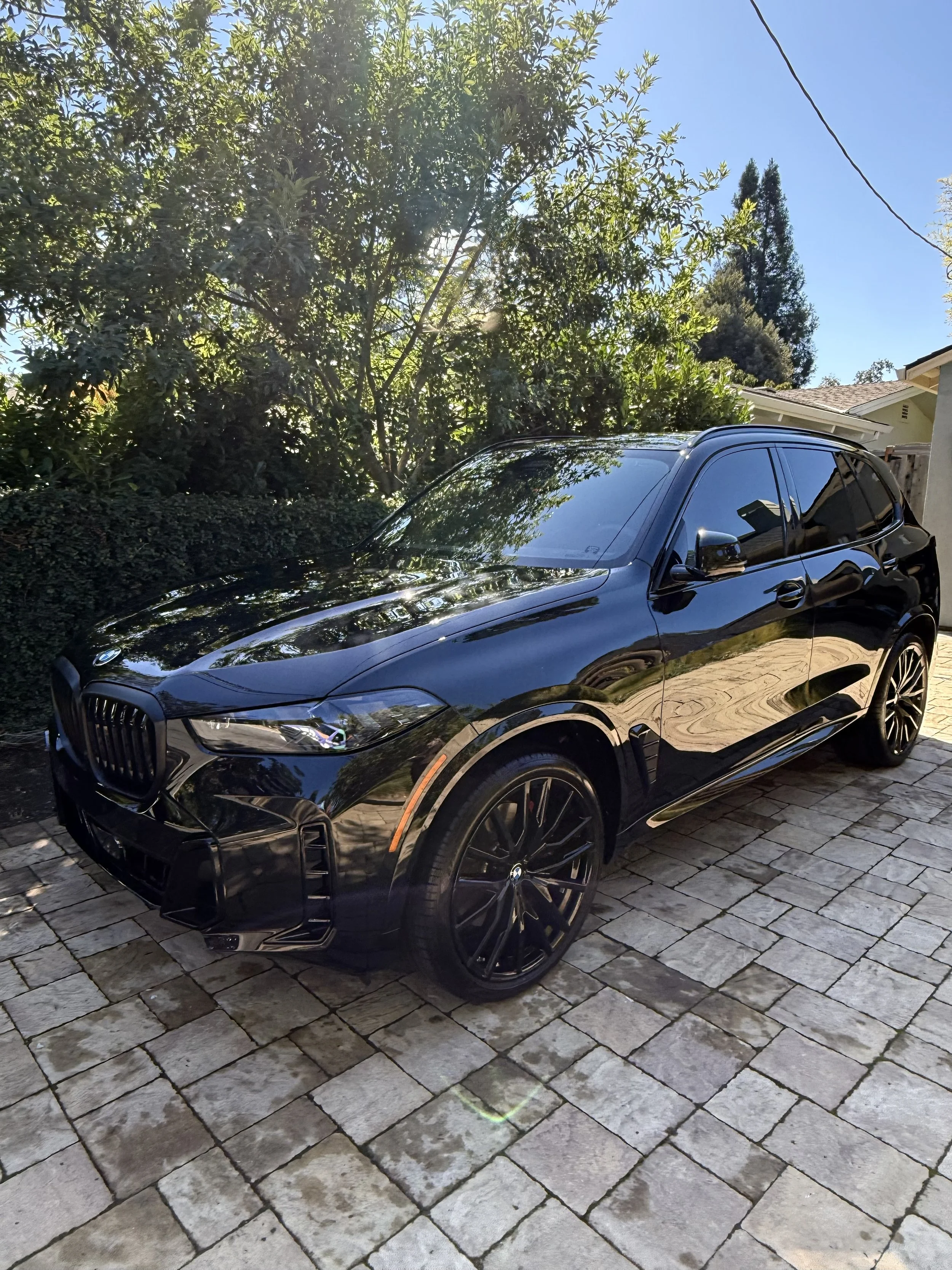 A shiny black BMW SUV parked on a stone driveway, car detailing in the Bay Area. 3 year Ceramic Coating and polish