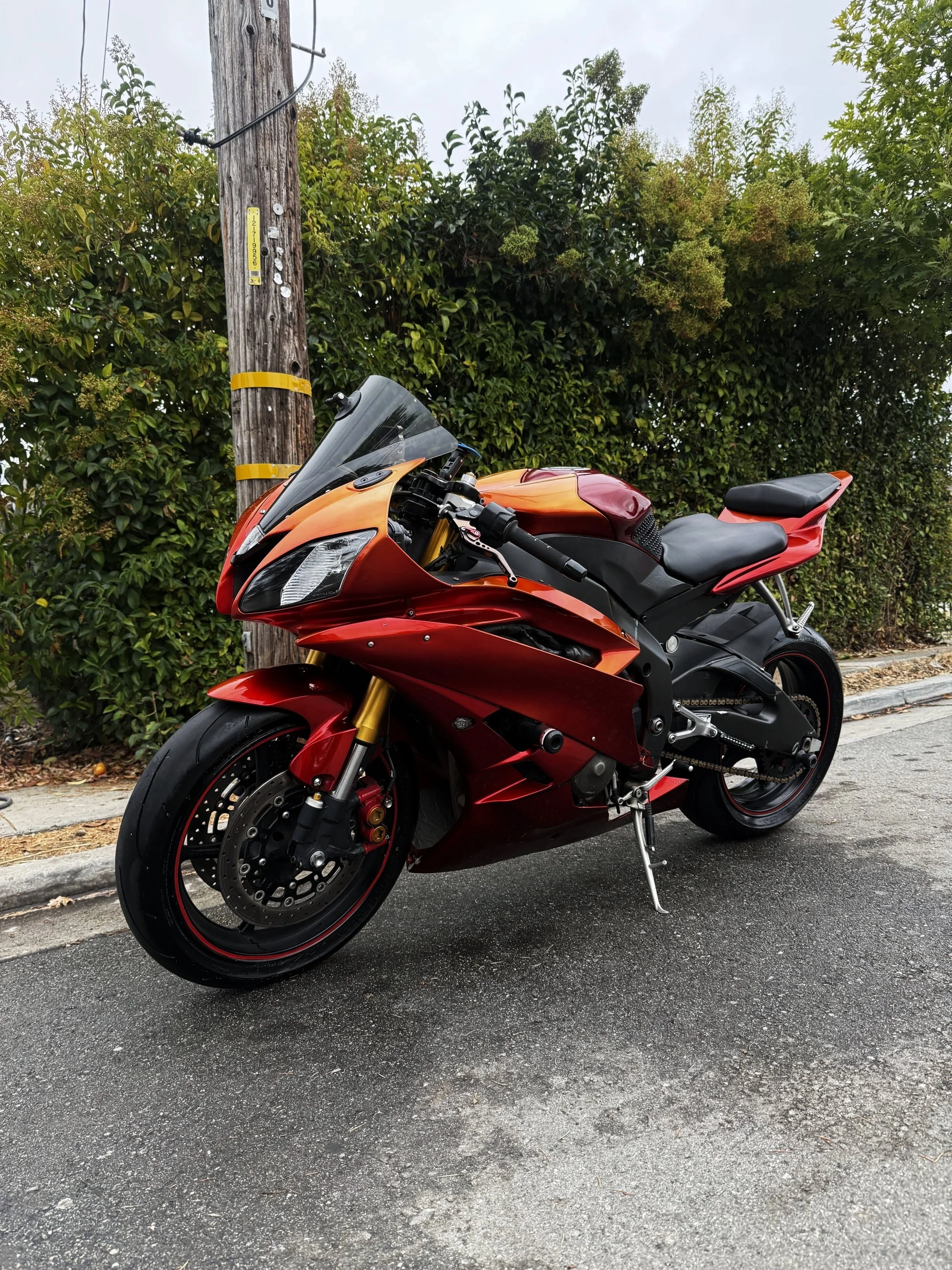 Red and black sport motorcycle parked on the street near a utility pole and green bushes