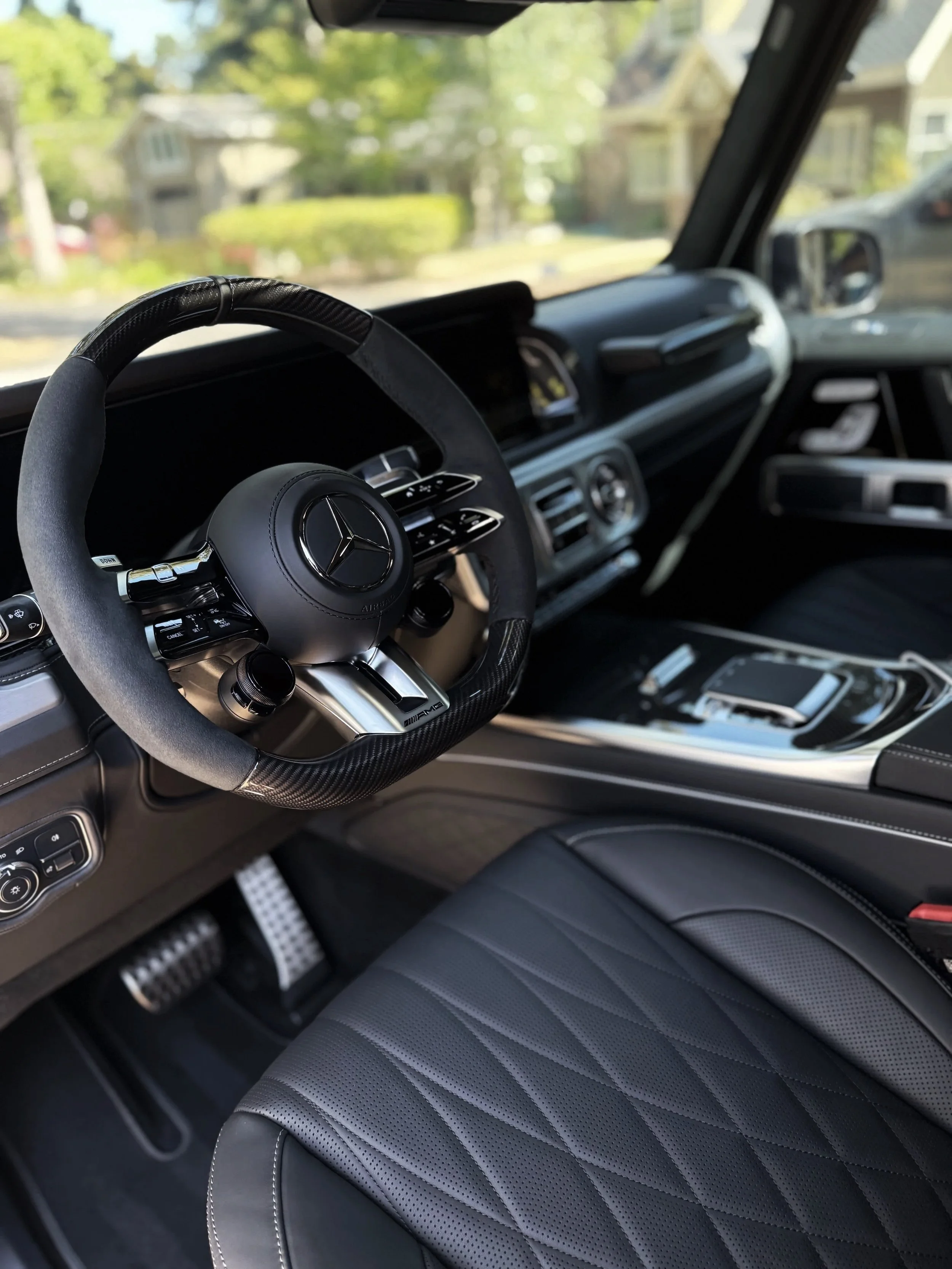 Interior of a Mercedes-Benz vehicle showing the steering wheel, dashboard, and front seat with black leather upholstery.