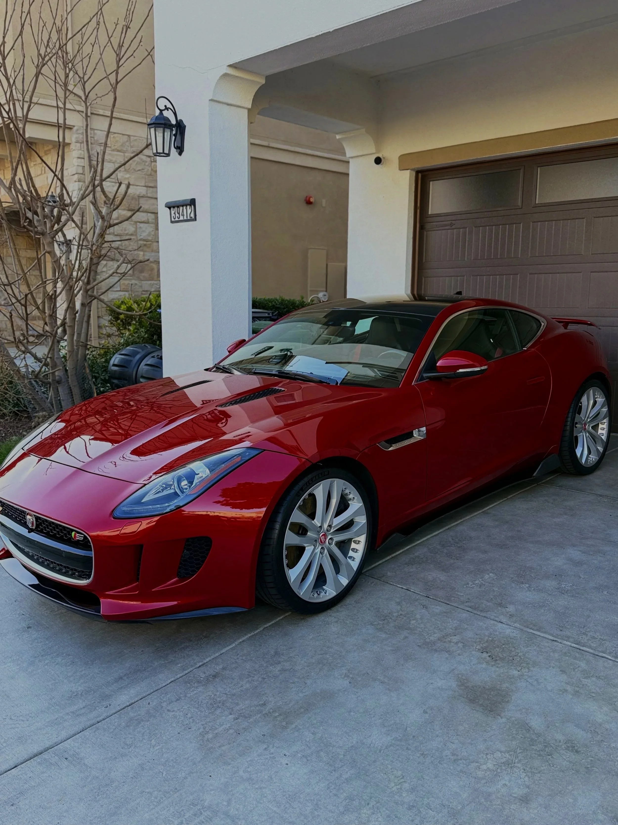 Red luxury sports car parked in front of a garage under a covered driveway.