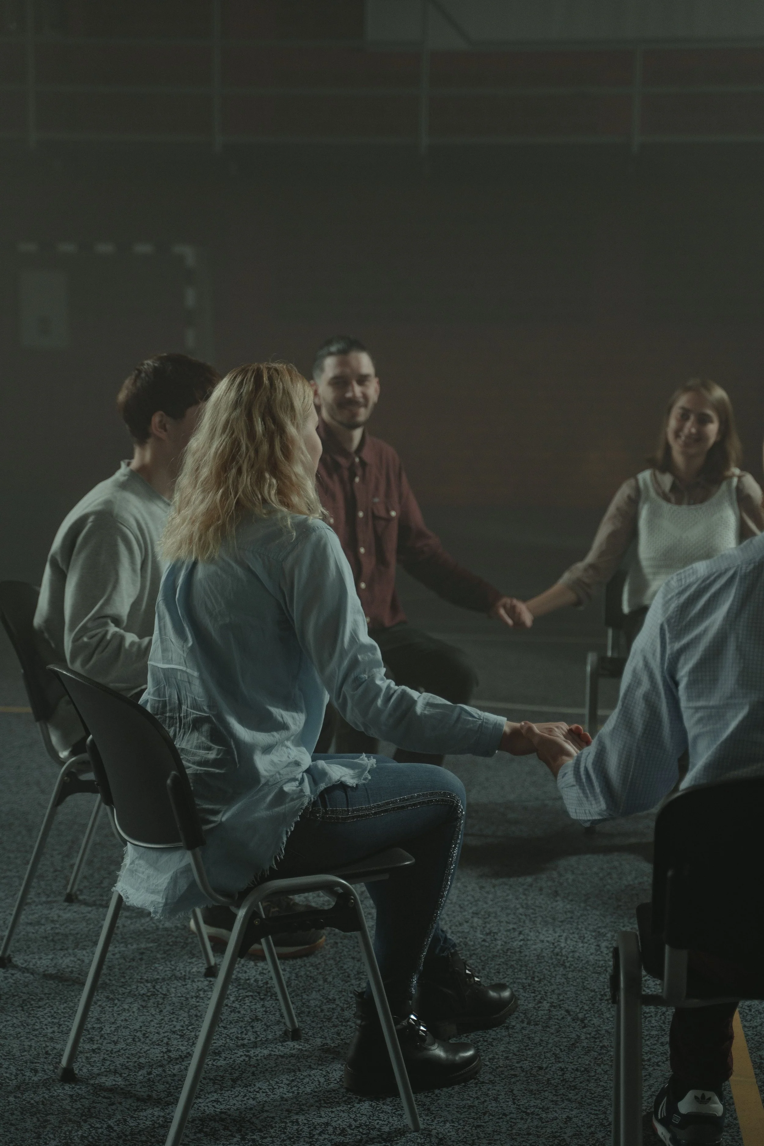 People sitting in a circle holding hands, participating in a group activity or discussion.