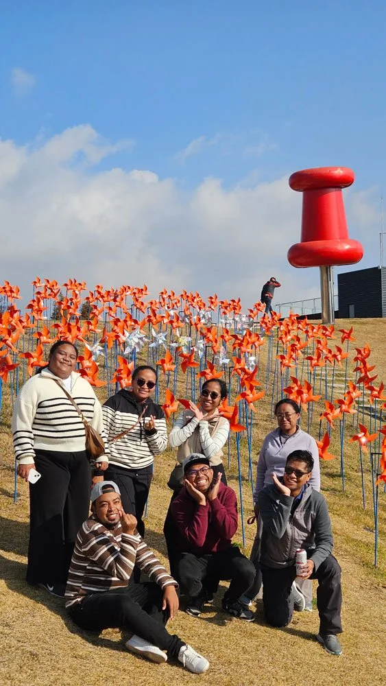 Madagascar travelers on a private tour at Pyeonghwa Nuri Park, panoramic view of open fields and sculptures, sunny day, vibrant travel photography
